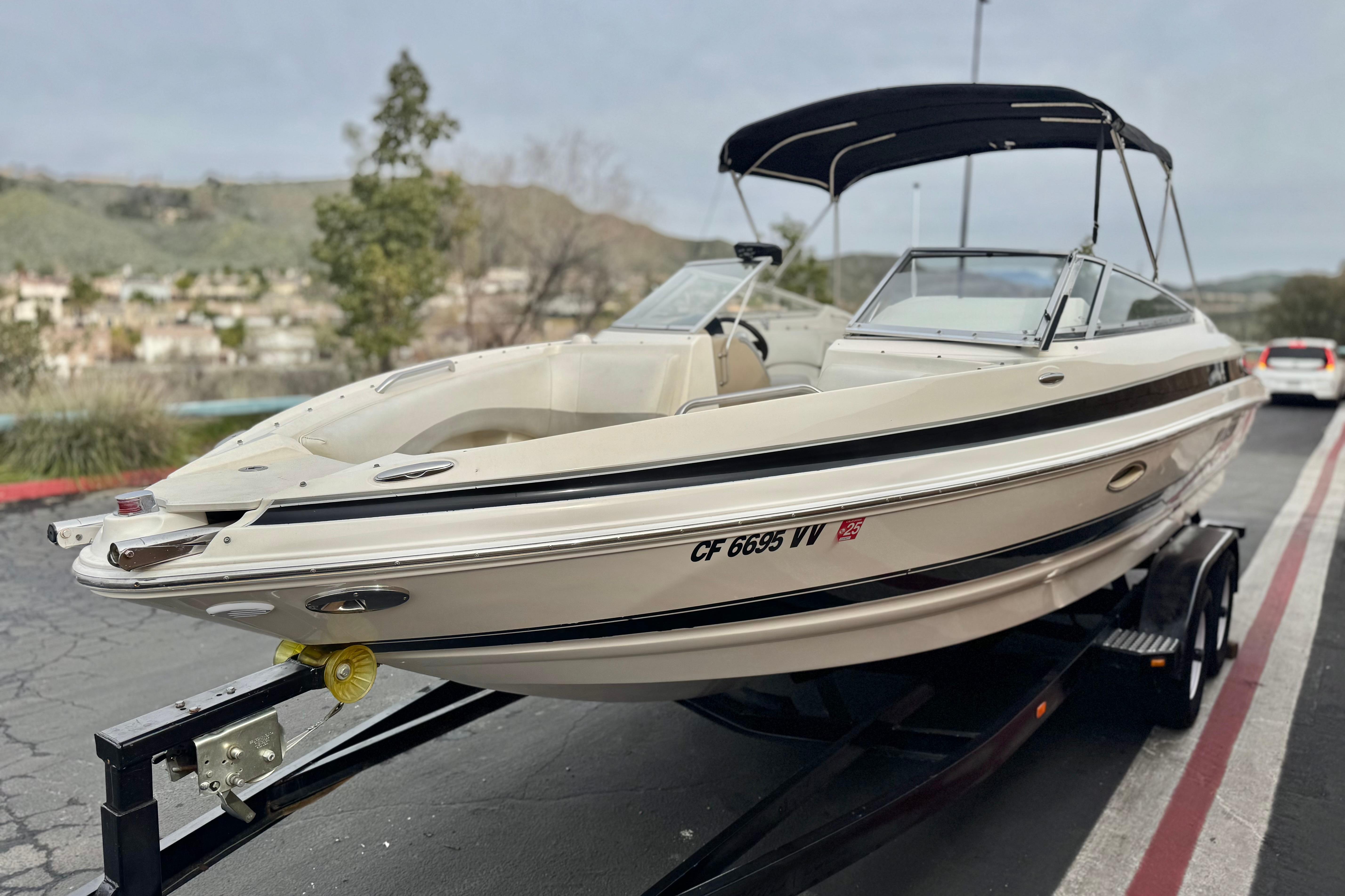 2006 Larson LXi 248 boat on trailer, parked on roadside with scenic background.