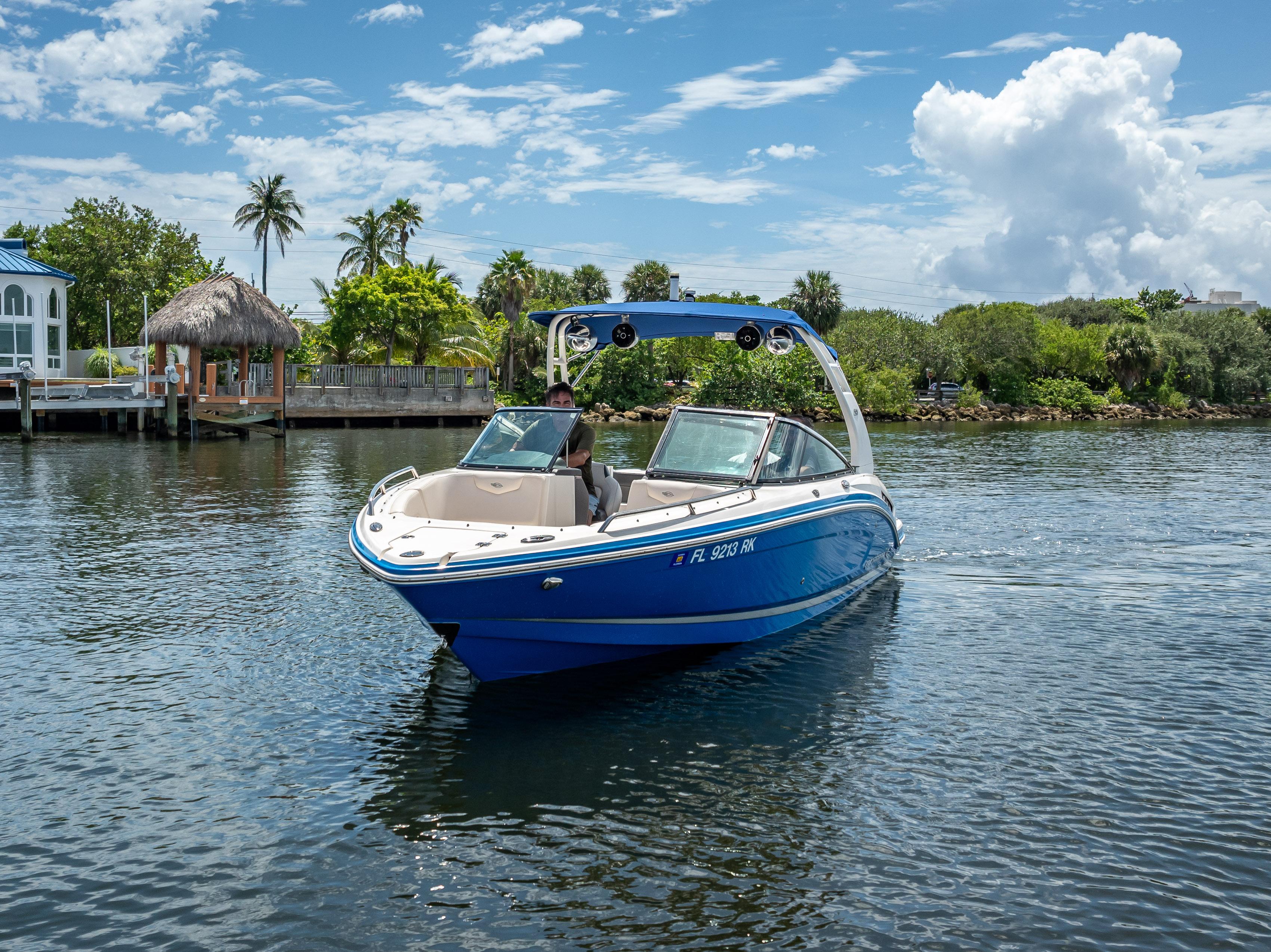 2017 Chaparral 227 SSX boat cruising on a sunny day near lush greenery and waterfront homes.