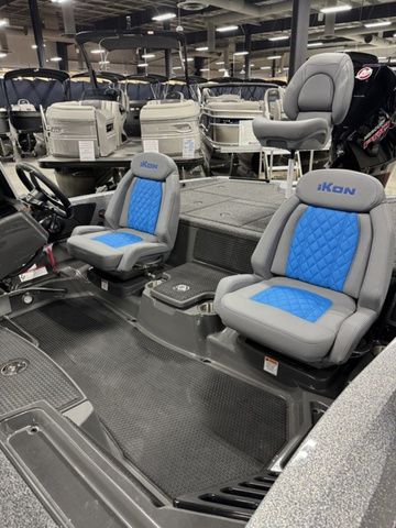 2026 Ikon Boats LXL20 interior with blue and gray seating, showcased in a boat showroom.