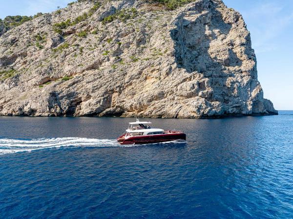 2025 Lagoon SIXTY 7 yacht cruising near a rocky cliff in clear blue waters.