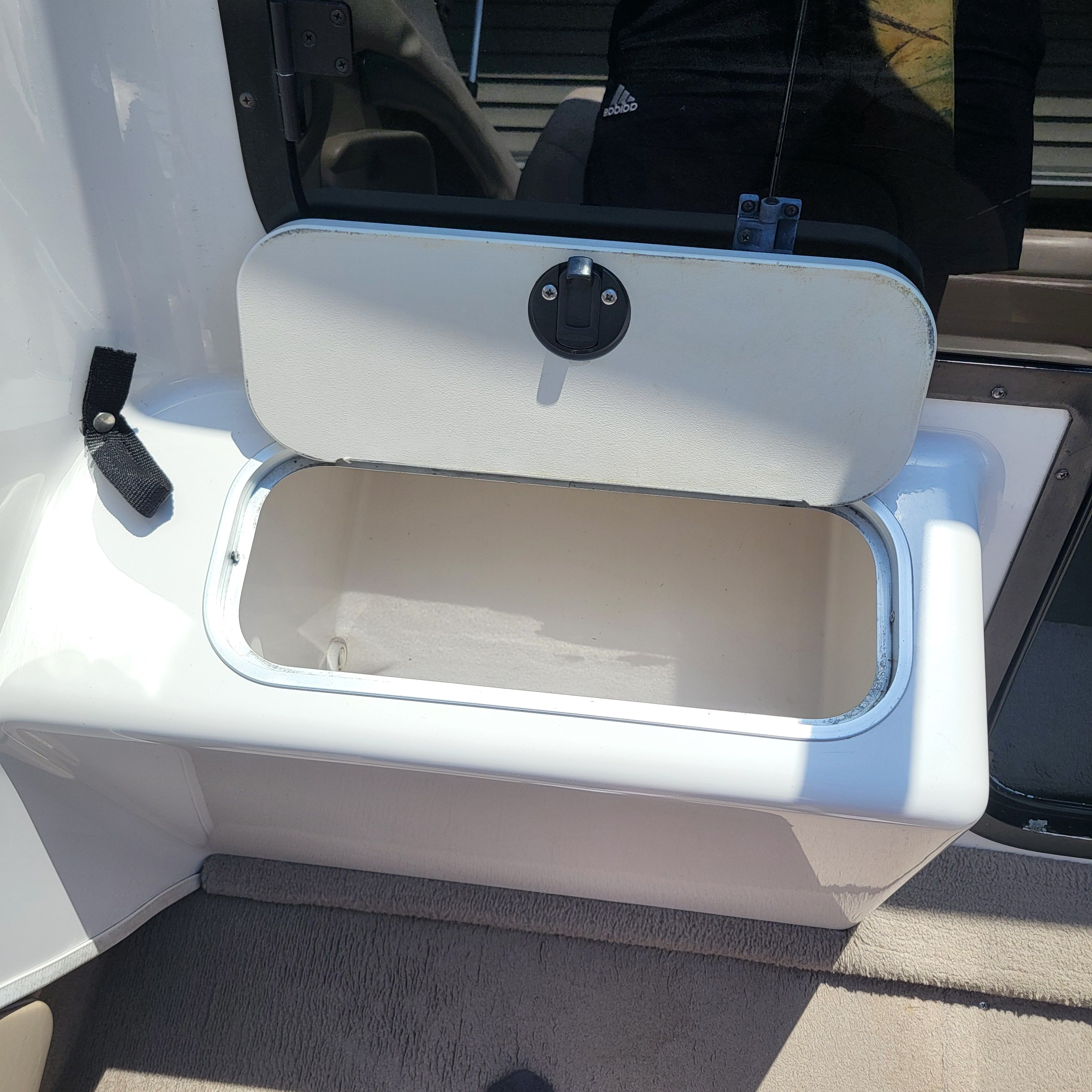 An open storage compartment on a boat with a white casing and black latch.