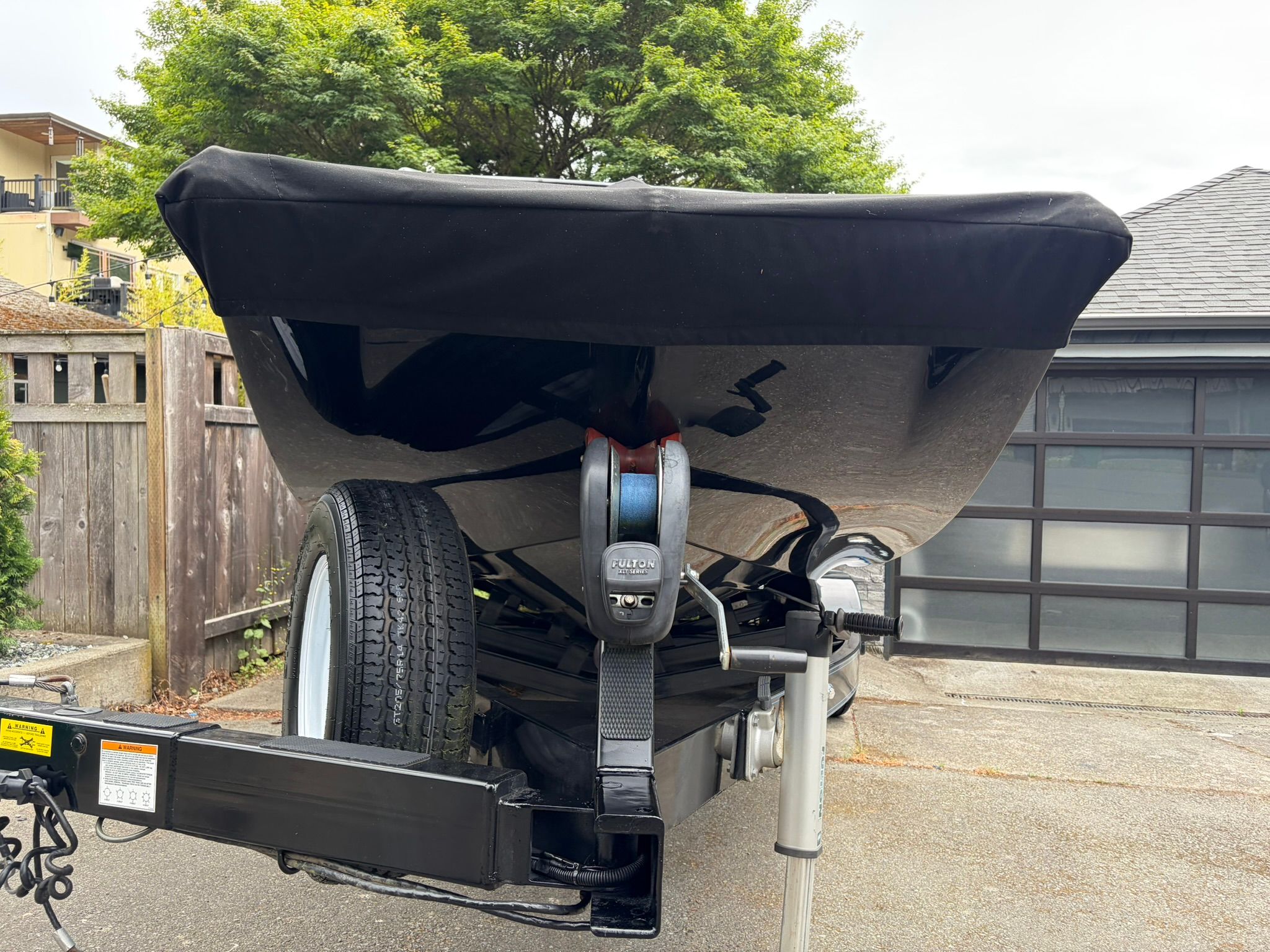 A 2016 Tigé RZ2 boat on a trailer, with a black cover, in a driveway.