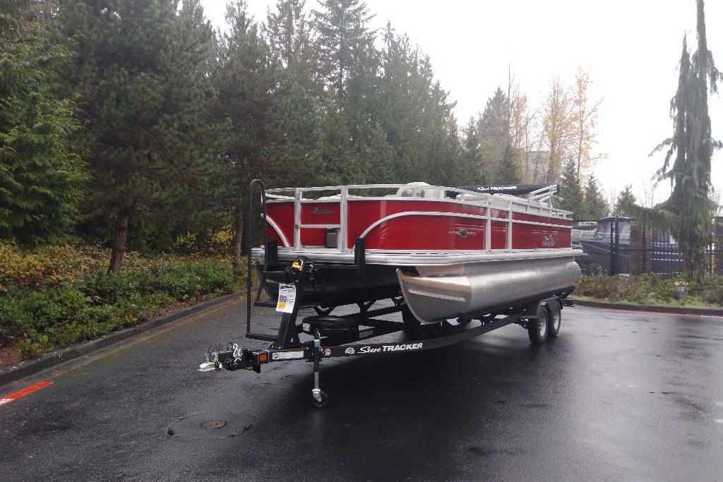 2026 Sun Tracker Fishin' Barge 22 DLX pontoon boat on trailer, surrounded by trees.