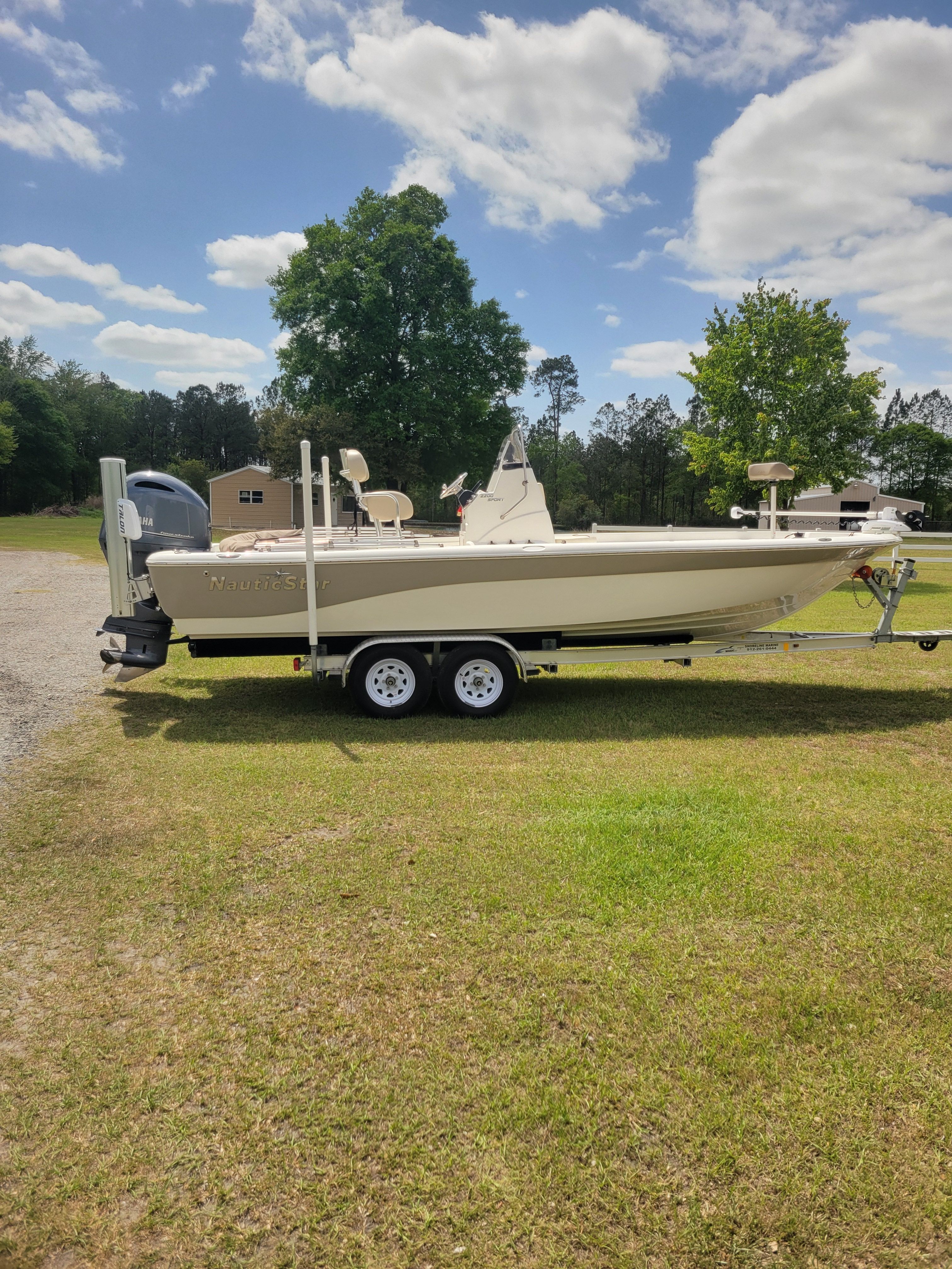 A NauticStar 2200 Sport boat on a trailer on grass under a blue sky.