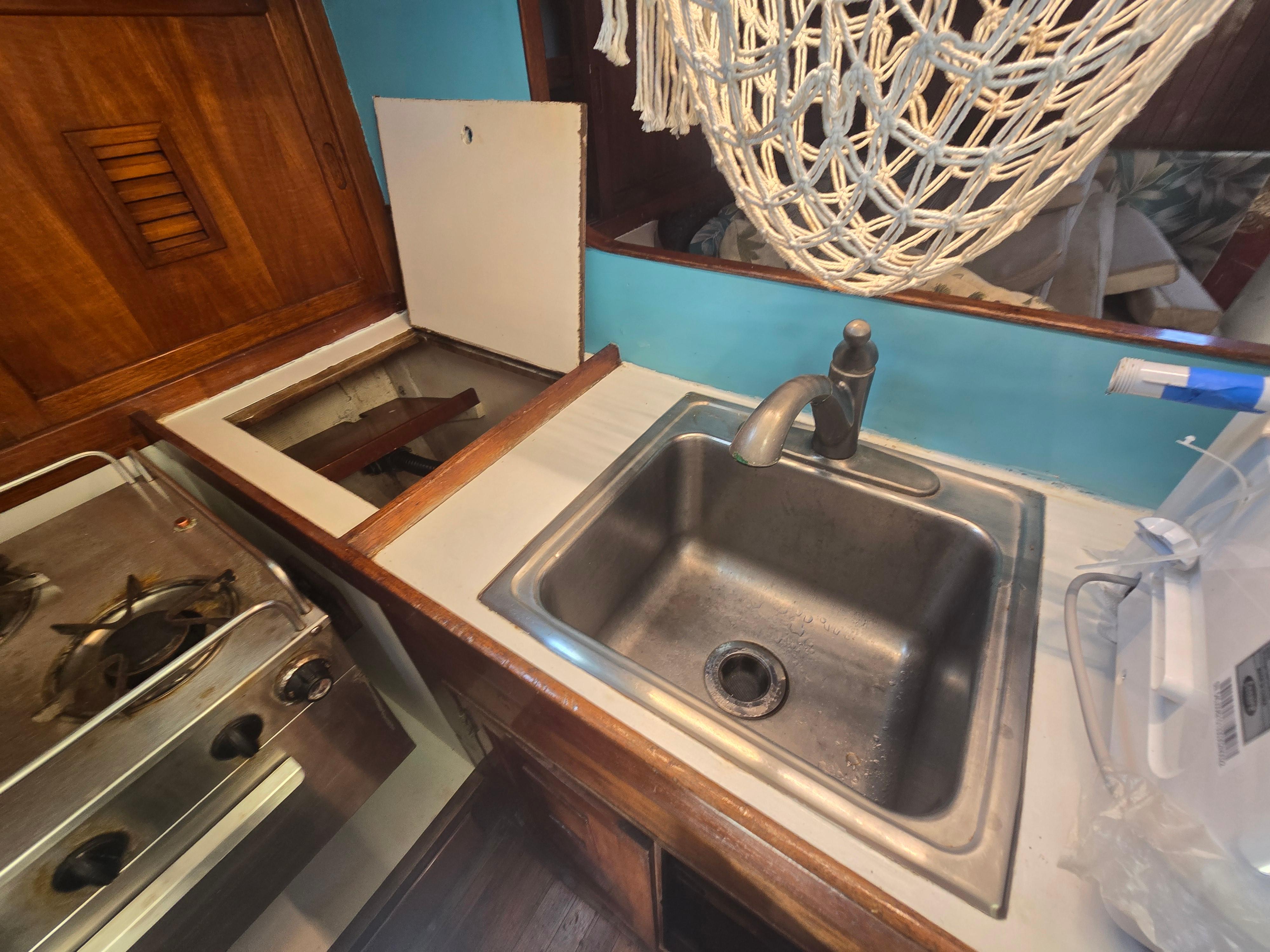 1978 Herreshoff 50 yacht kitchen with sink, stove, and wooden cabinetry.