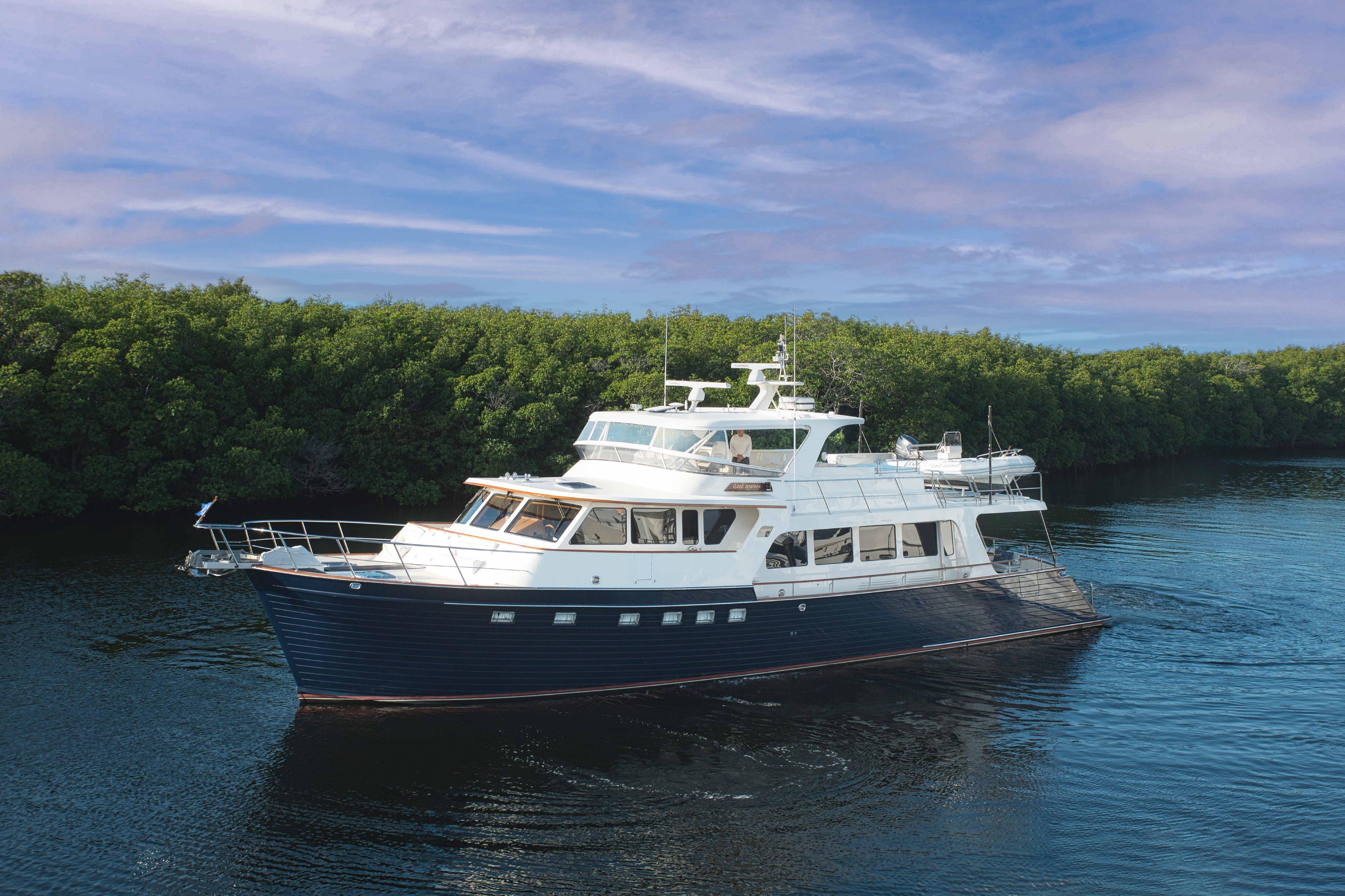 Luxurious 2009 Marlow 78E yacht cruising on calm waters near lush greenery.