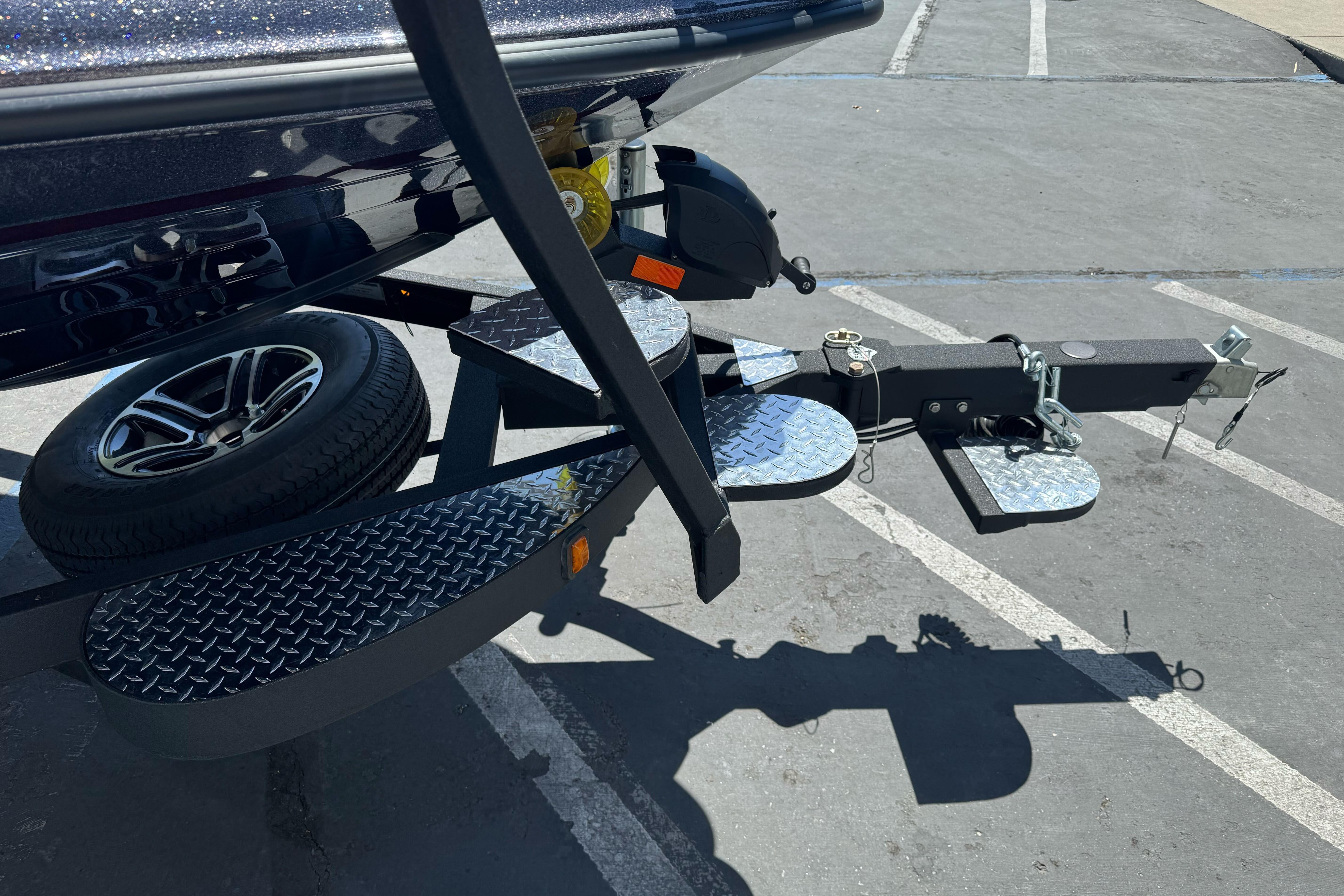 2026 Triton 18 TrX boat trailer with diamond plate steps and spare tire in parking lot.