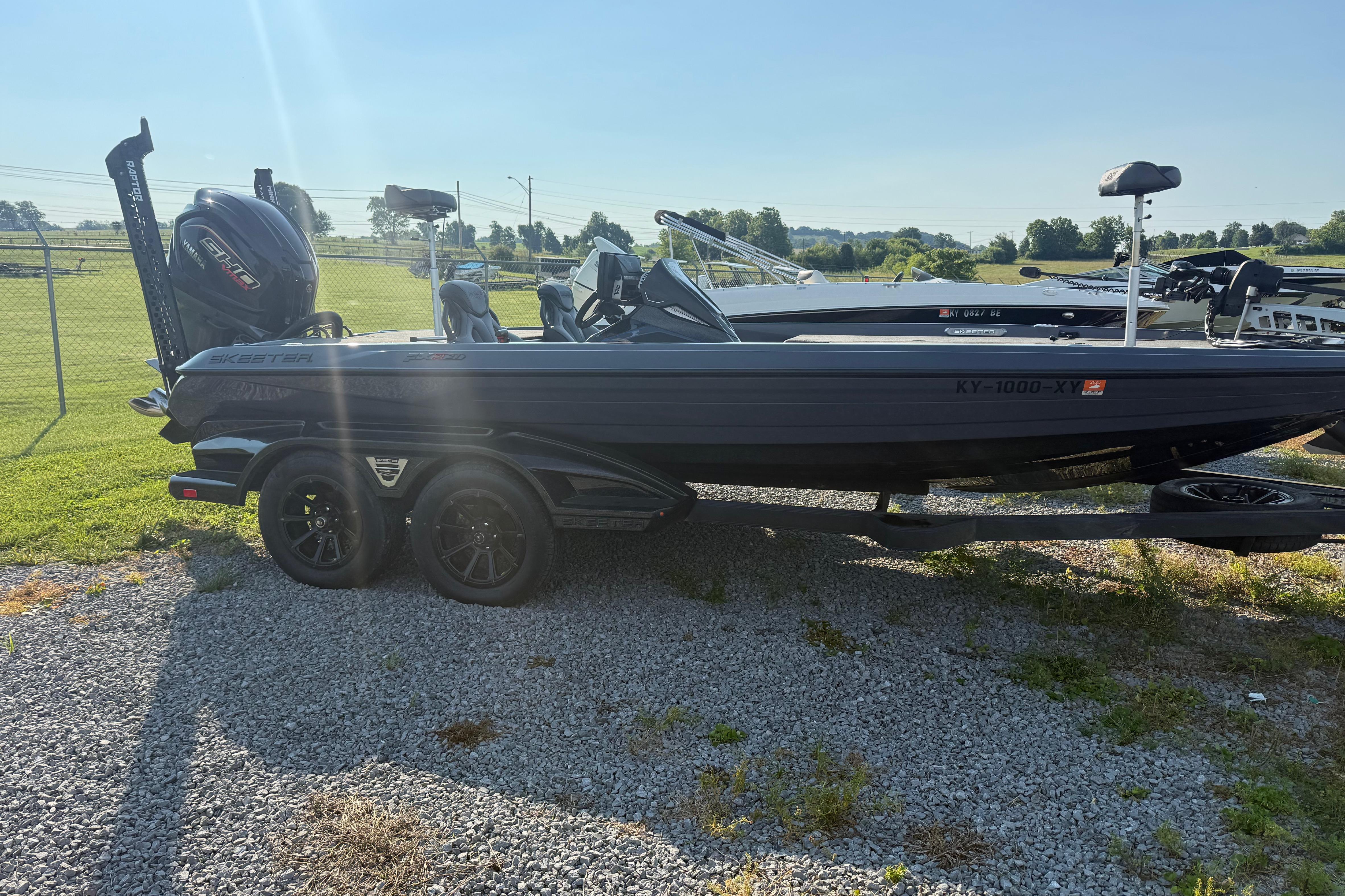 2024 Skeeter FXR21 boat on trailer, parked on gravel, with outboard motor.