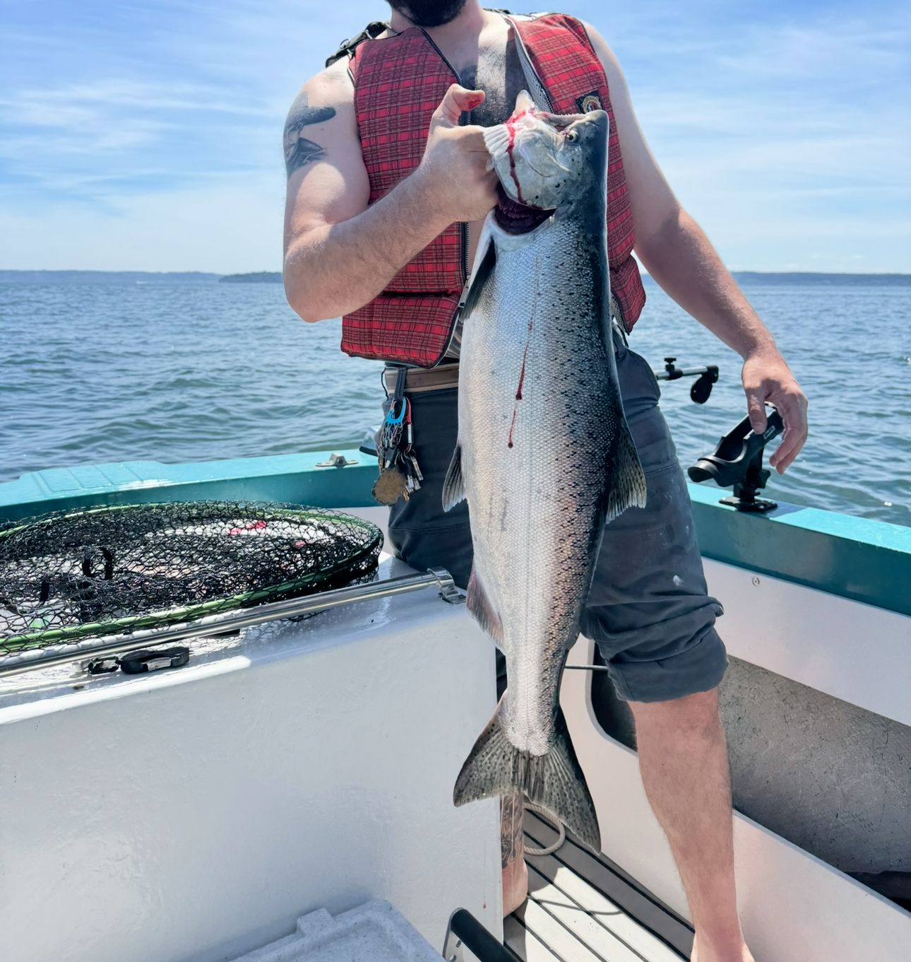 A man holds a large fish on a boat. He is wearing a red life jacket.