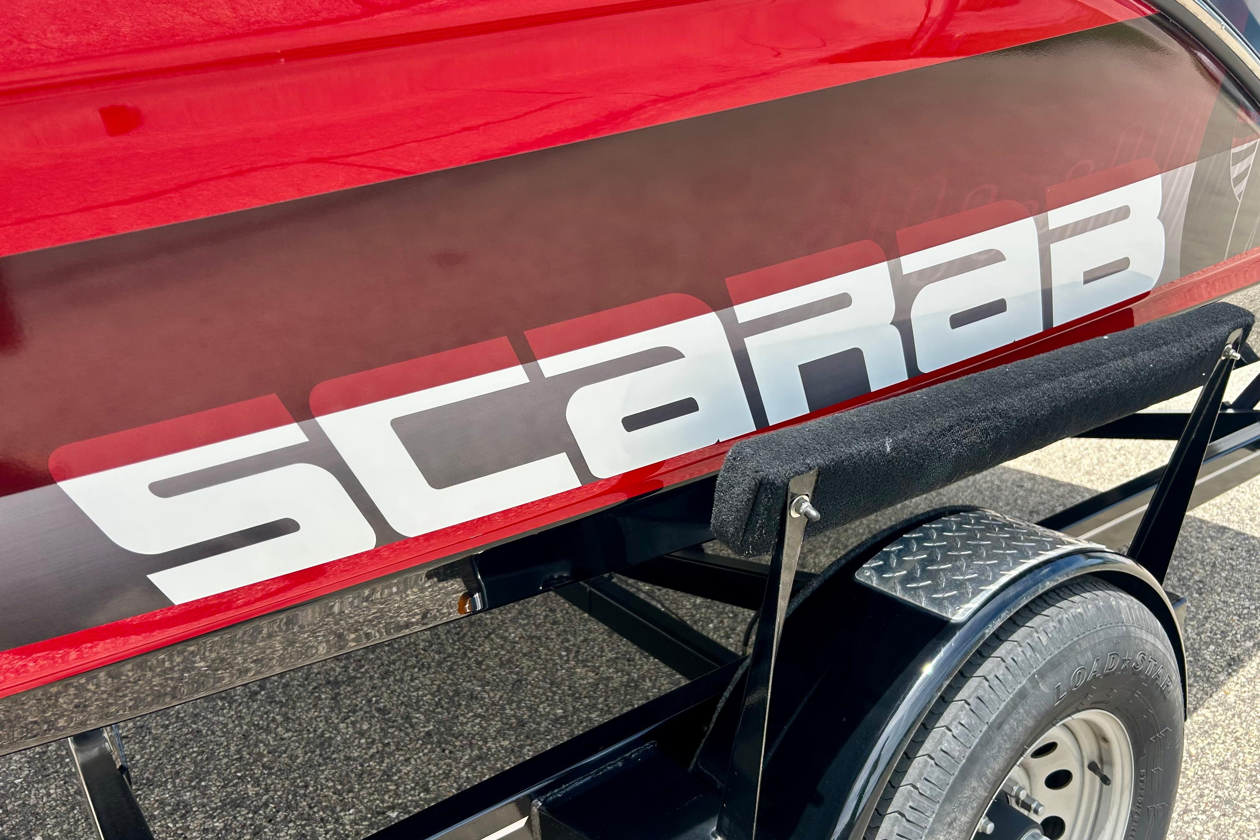 Red 2021 Scarab 195 ID boat on trailer, showcasing bold logo design.