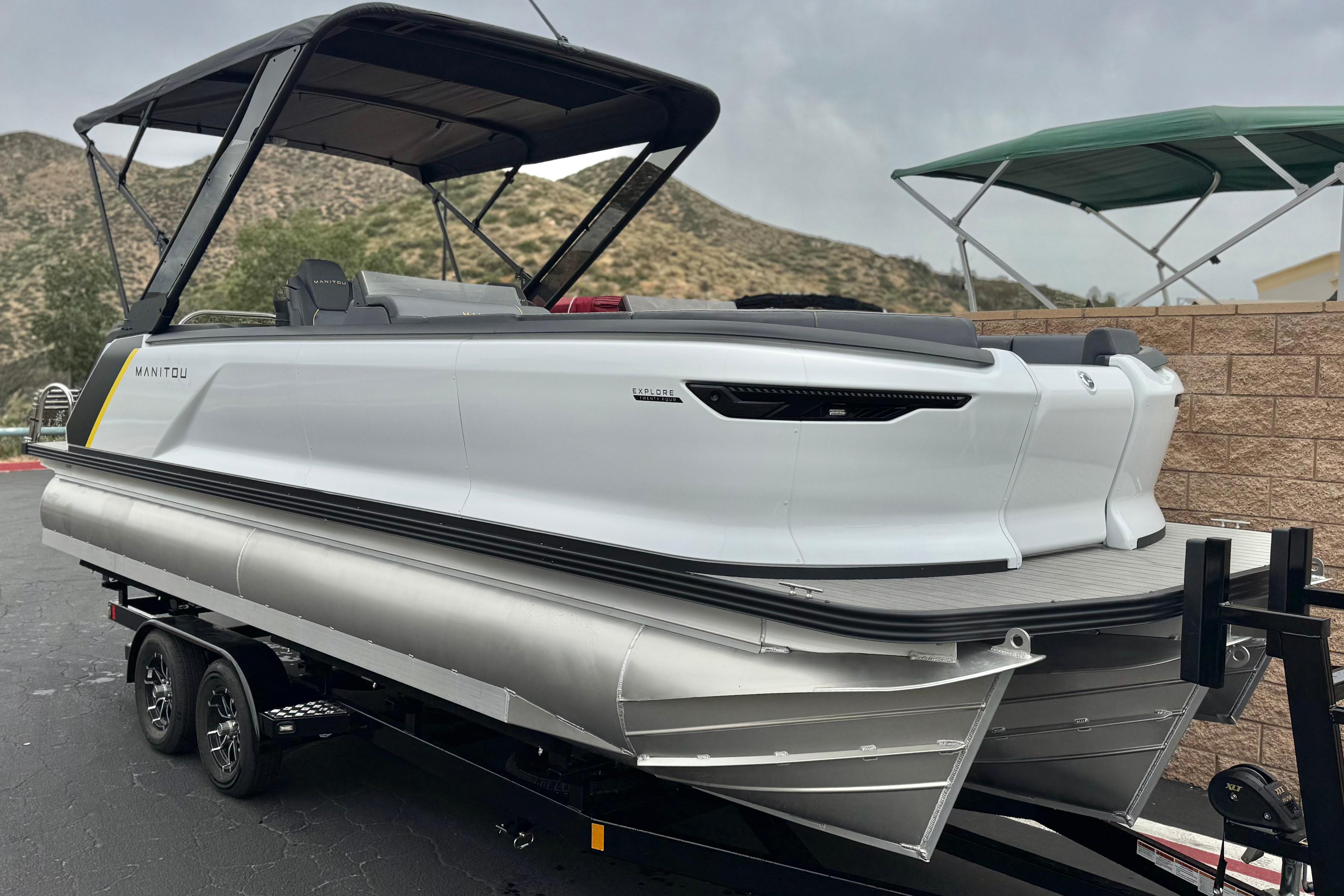 2025 Manitou EXPLORE 24 pontoon boat on trailer, sleek design, mountainous backdrop.