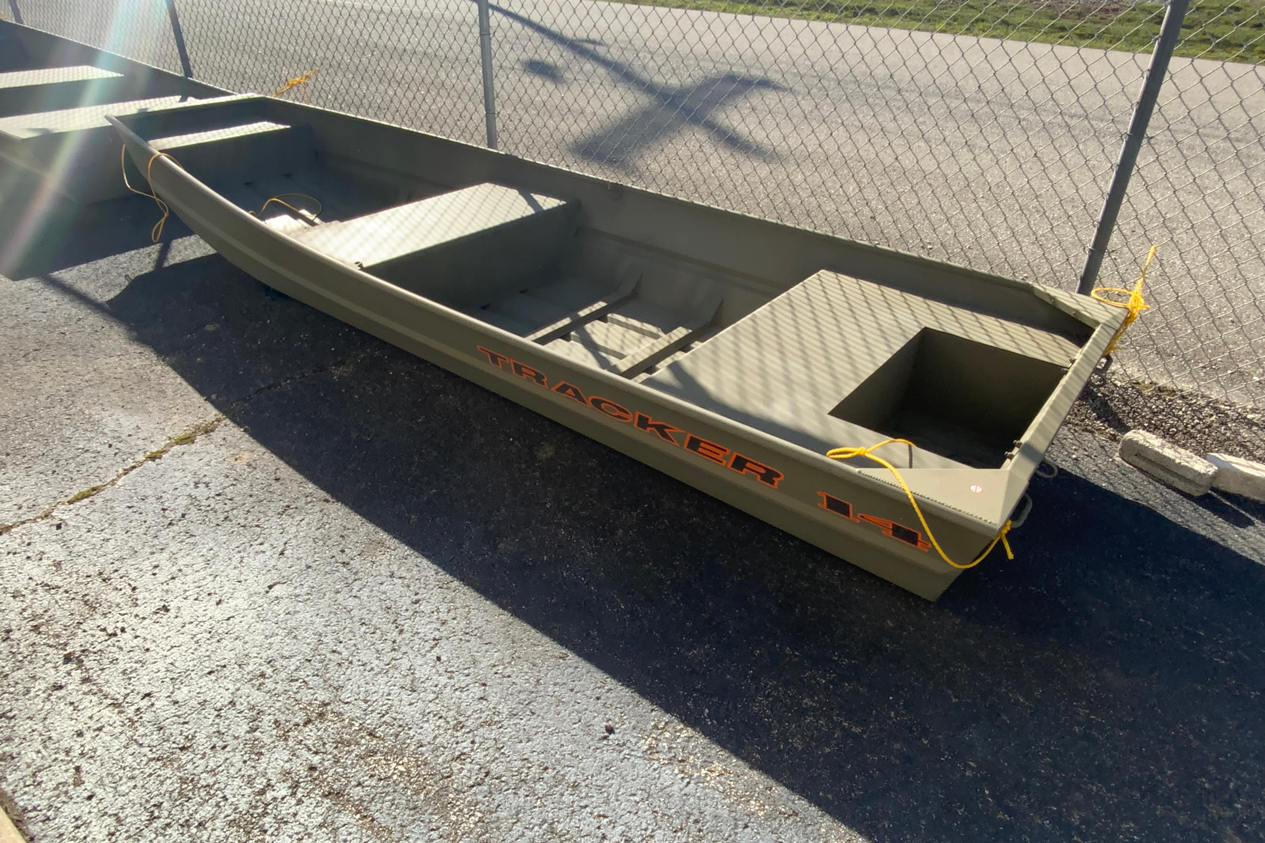 2026 Tracker Grizzly 14 Jon boat parked on pavement near chain-link fence.