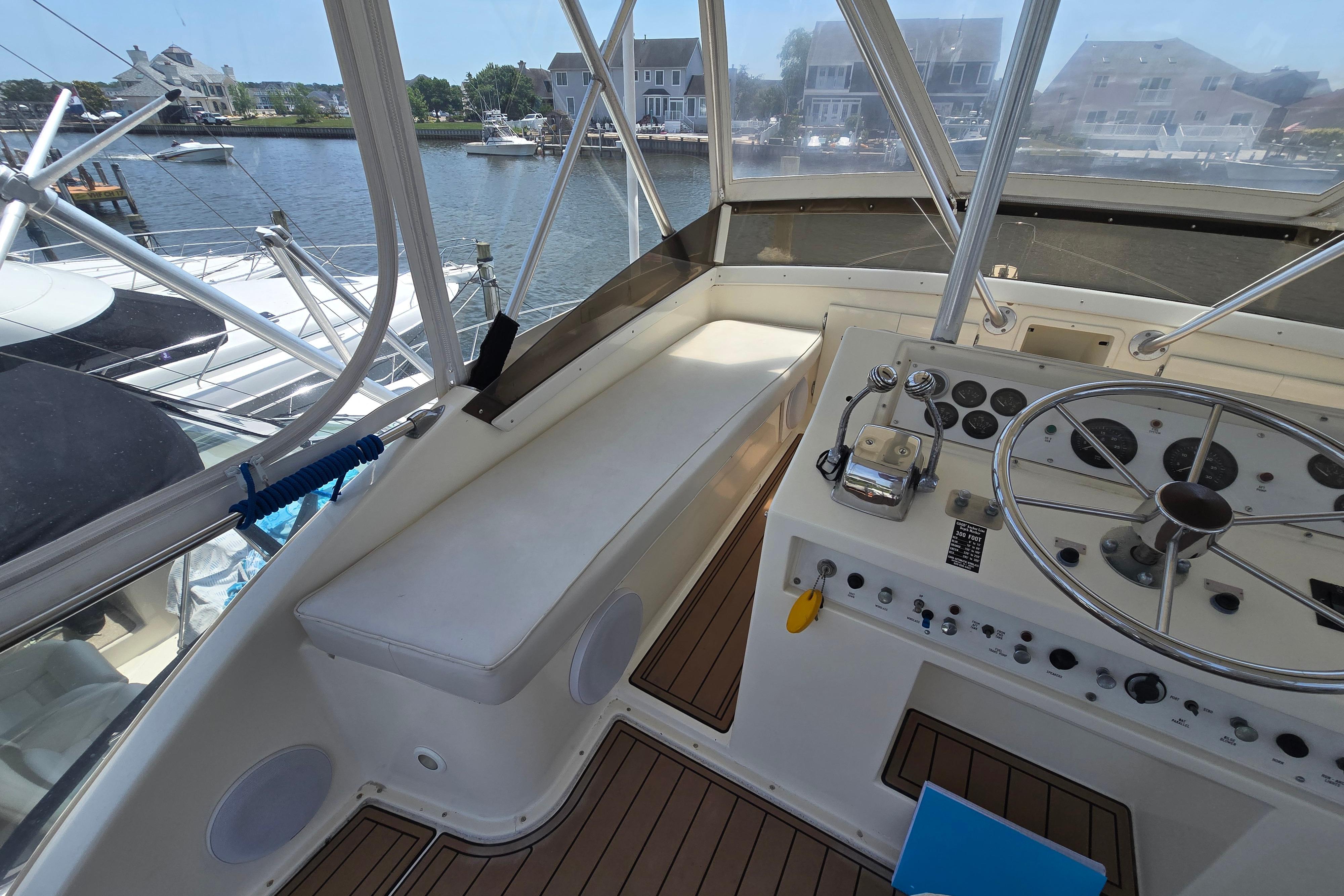 1988 Post 46 Convertible yacht cockpit with steering wheel, controls, and seating, docked by waterfront homes.
