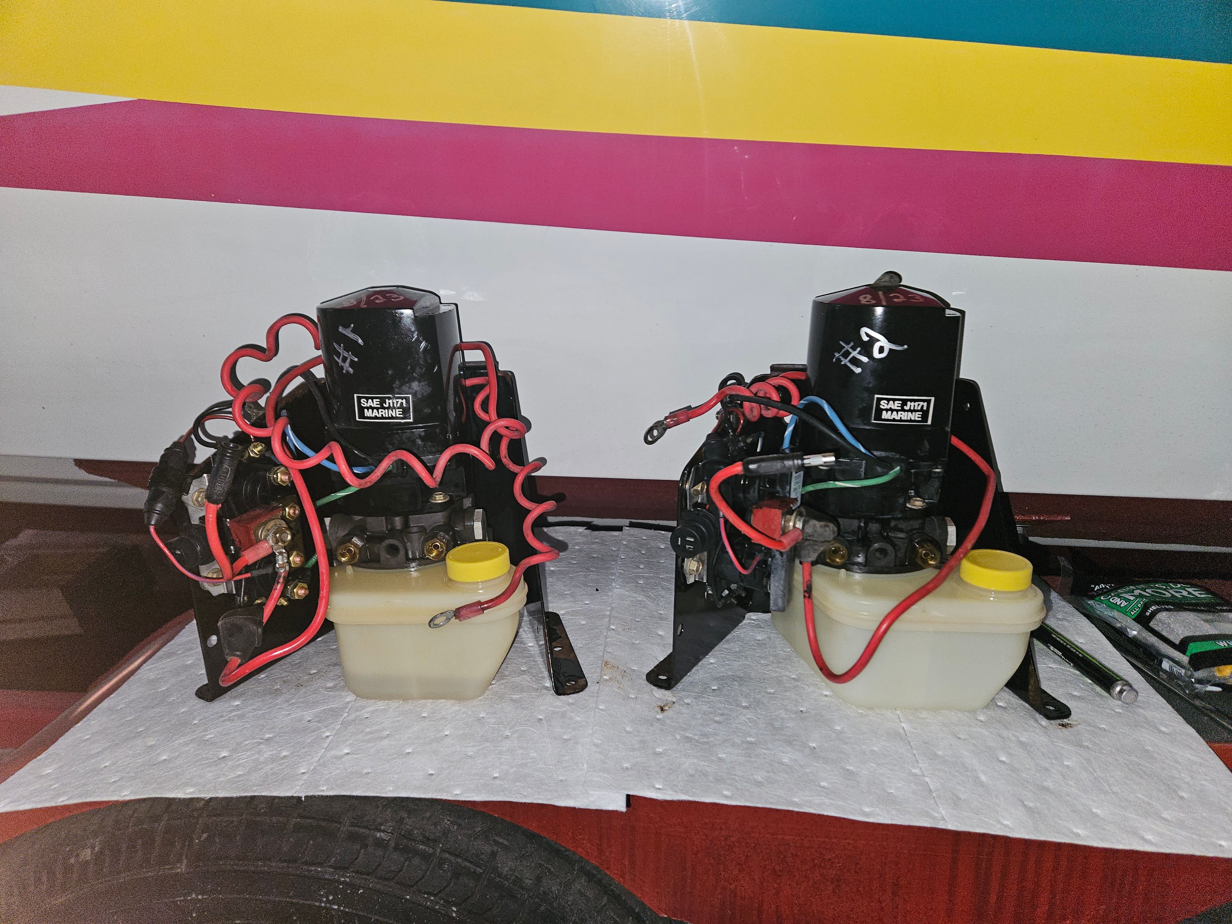 Two boat engines with red wires and yellow fluid reservoirs on a workbench.