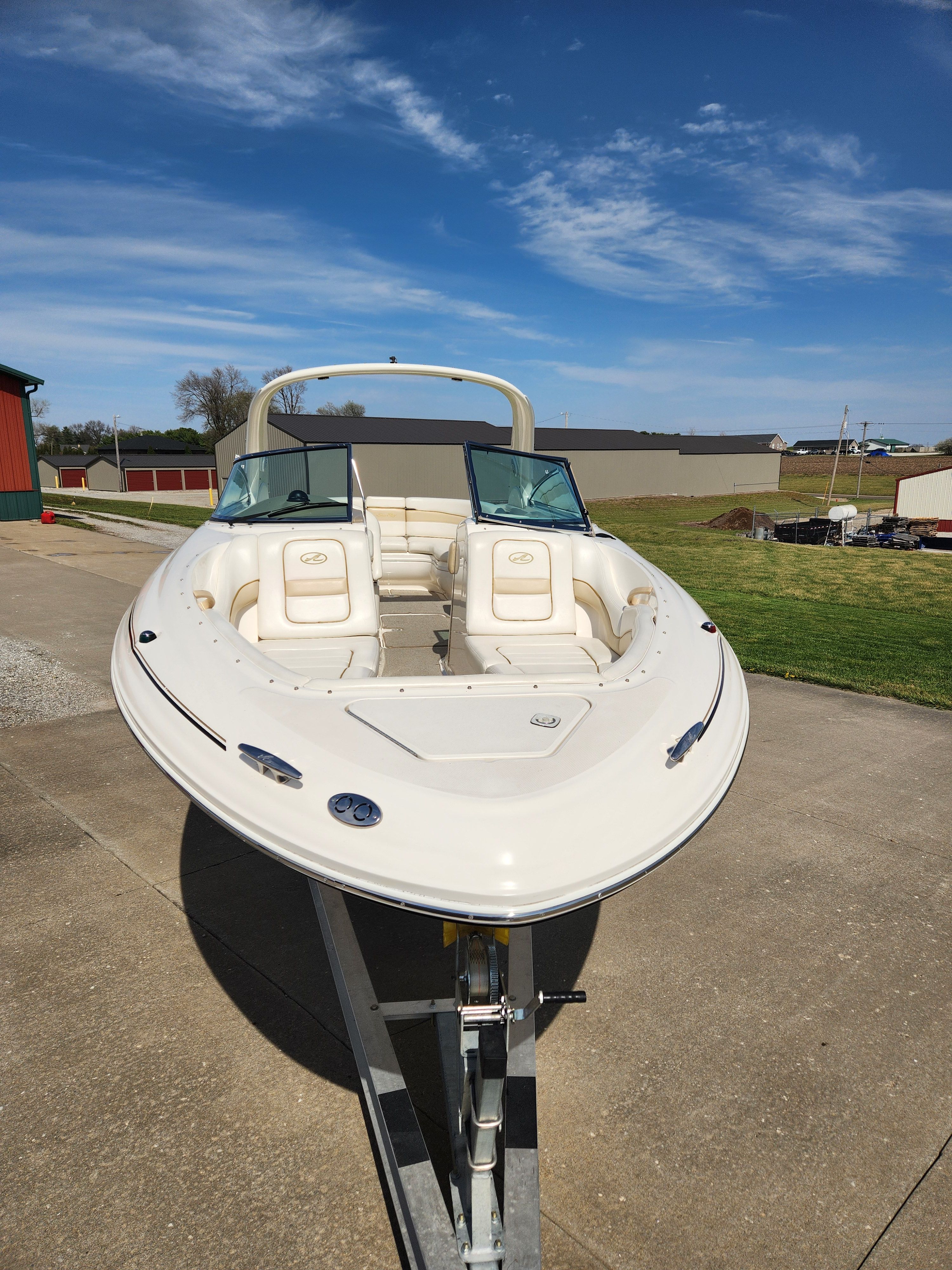 A white motorboat on a trailer, featuring two seats and a blue sky background.