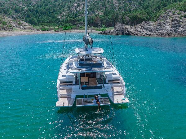 2025 Lagoon 51 ICONIC yacht anchored in turquoise waters near rocky coastline.