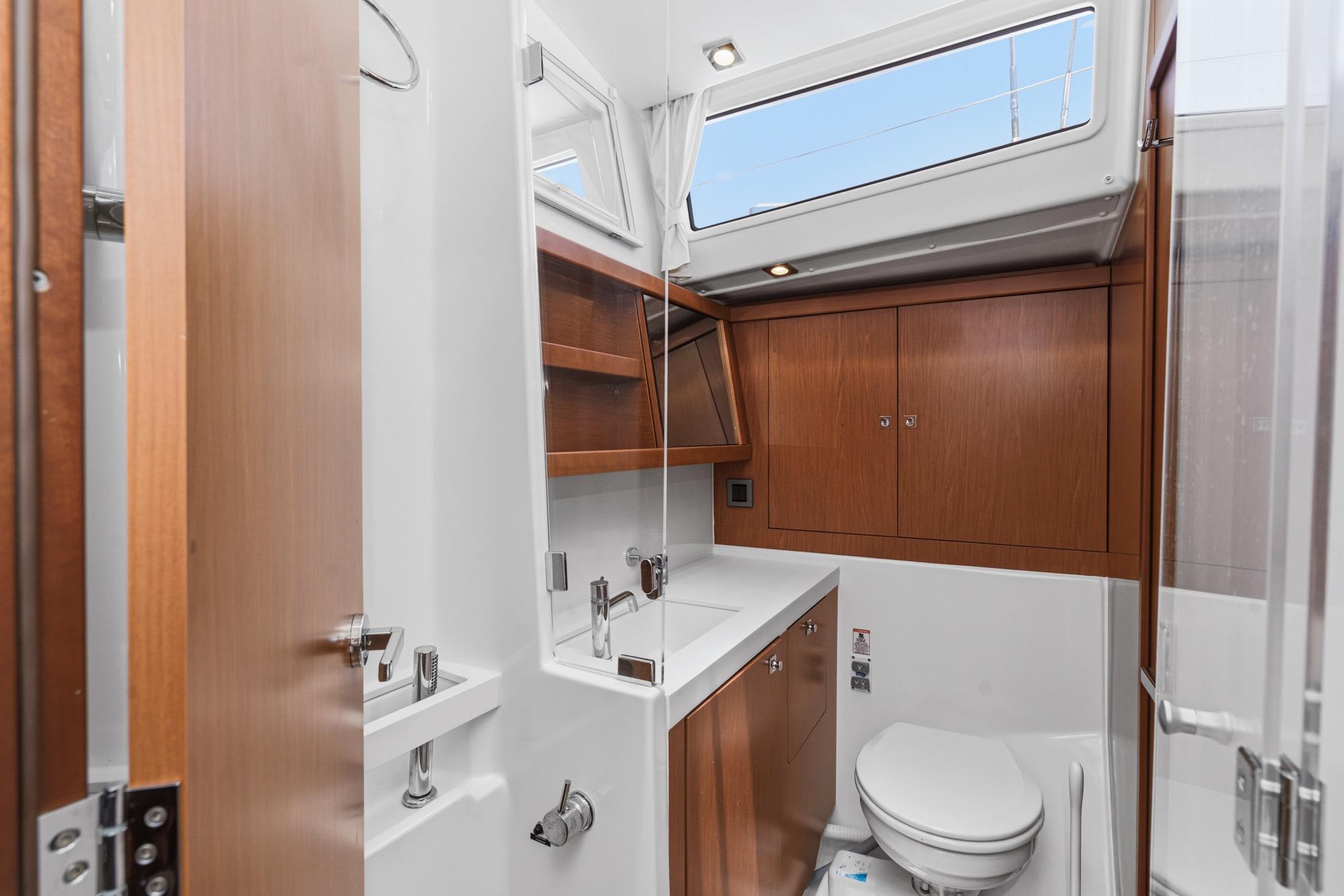 Modern bathroom interior of 2017 Beneteau Sense 50 yacht, featuring wood cabinetry and sleek fixtures.