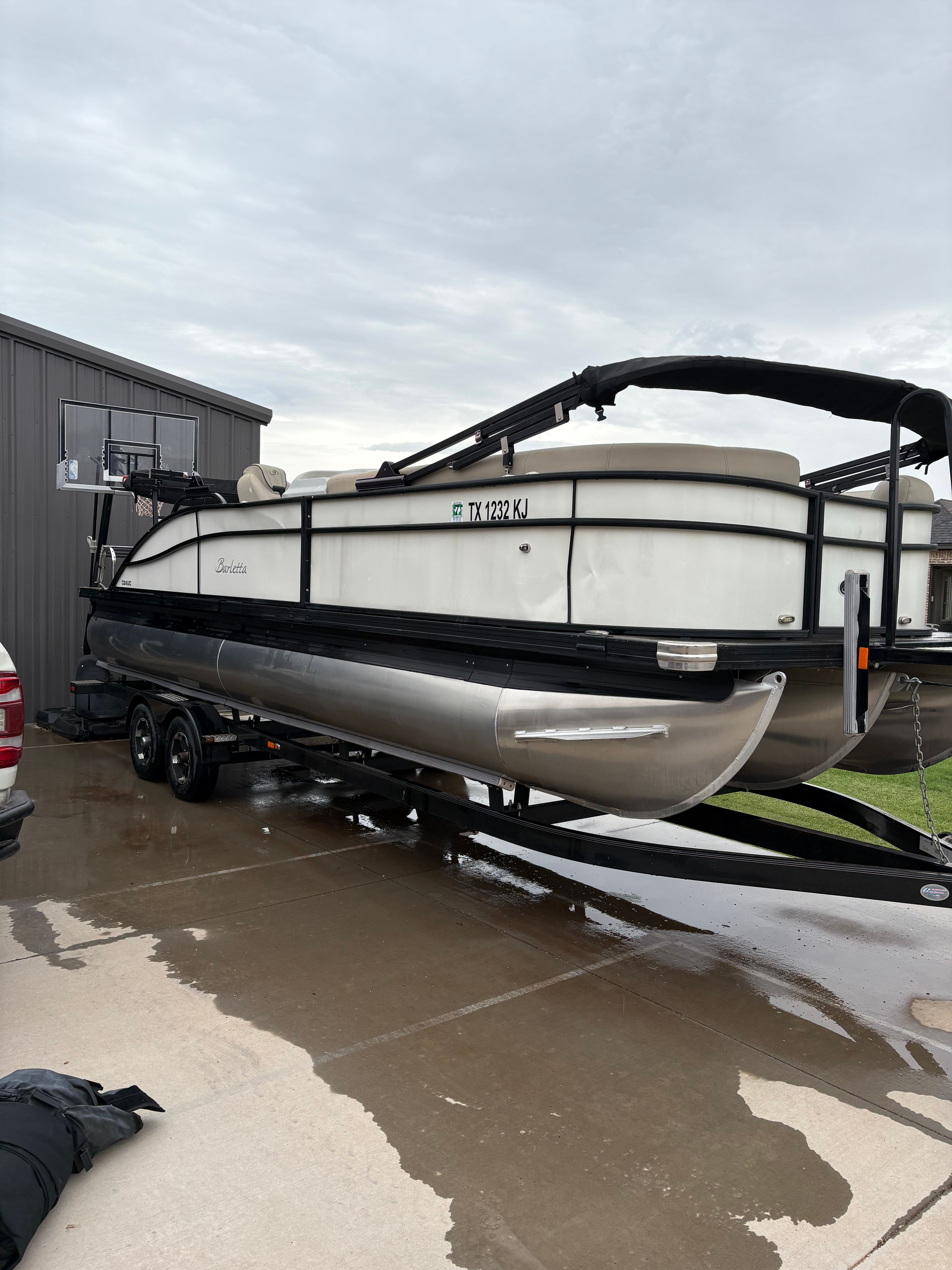 A 2021 Barletta C24UC pontoon boat on a trailer next to a building.