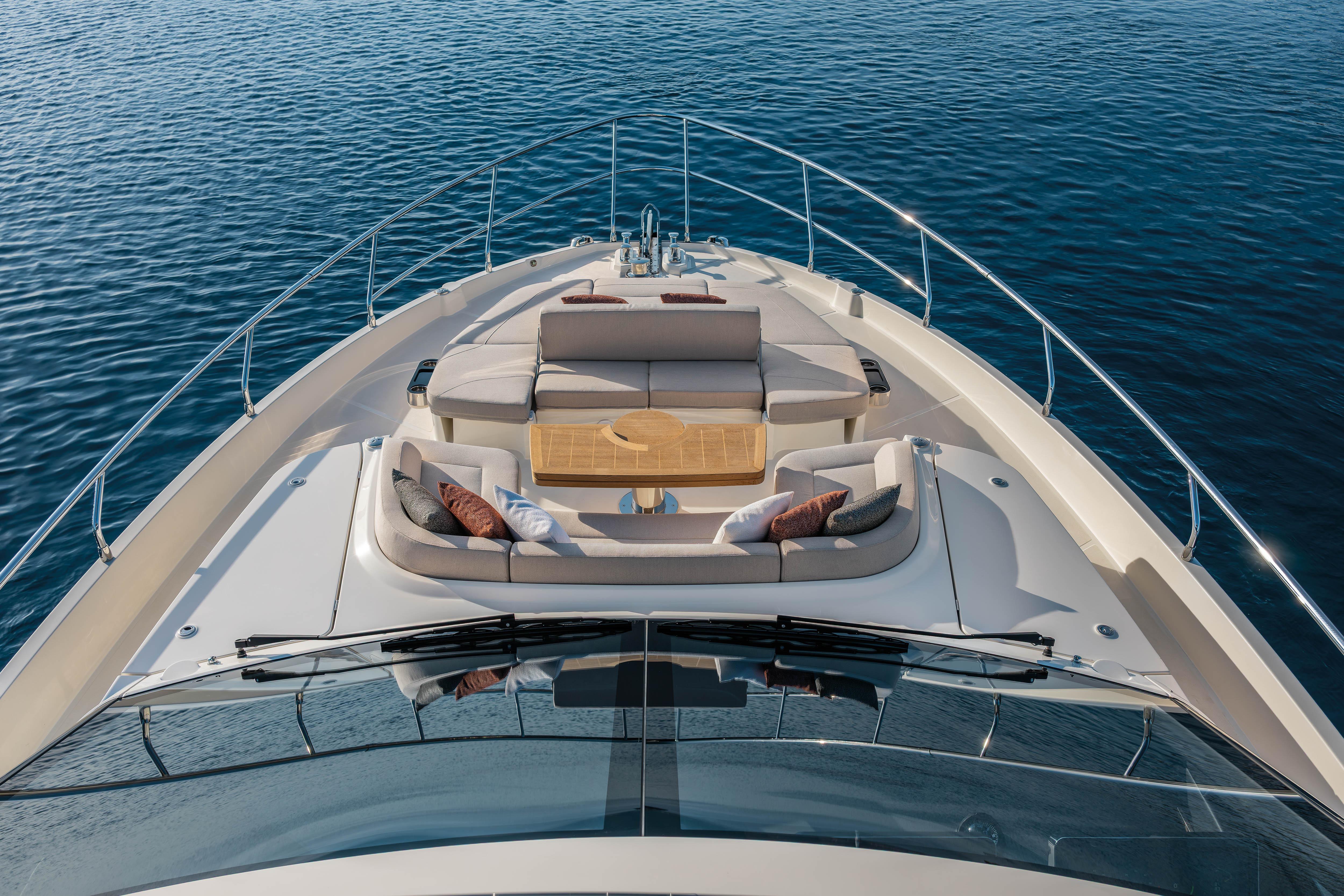 Luxurious yacht sun deck with cushions and table, surrounded by calm water.