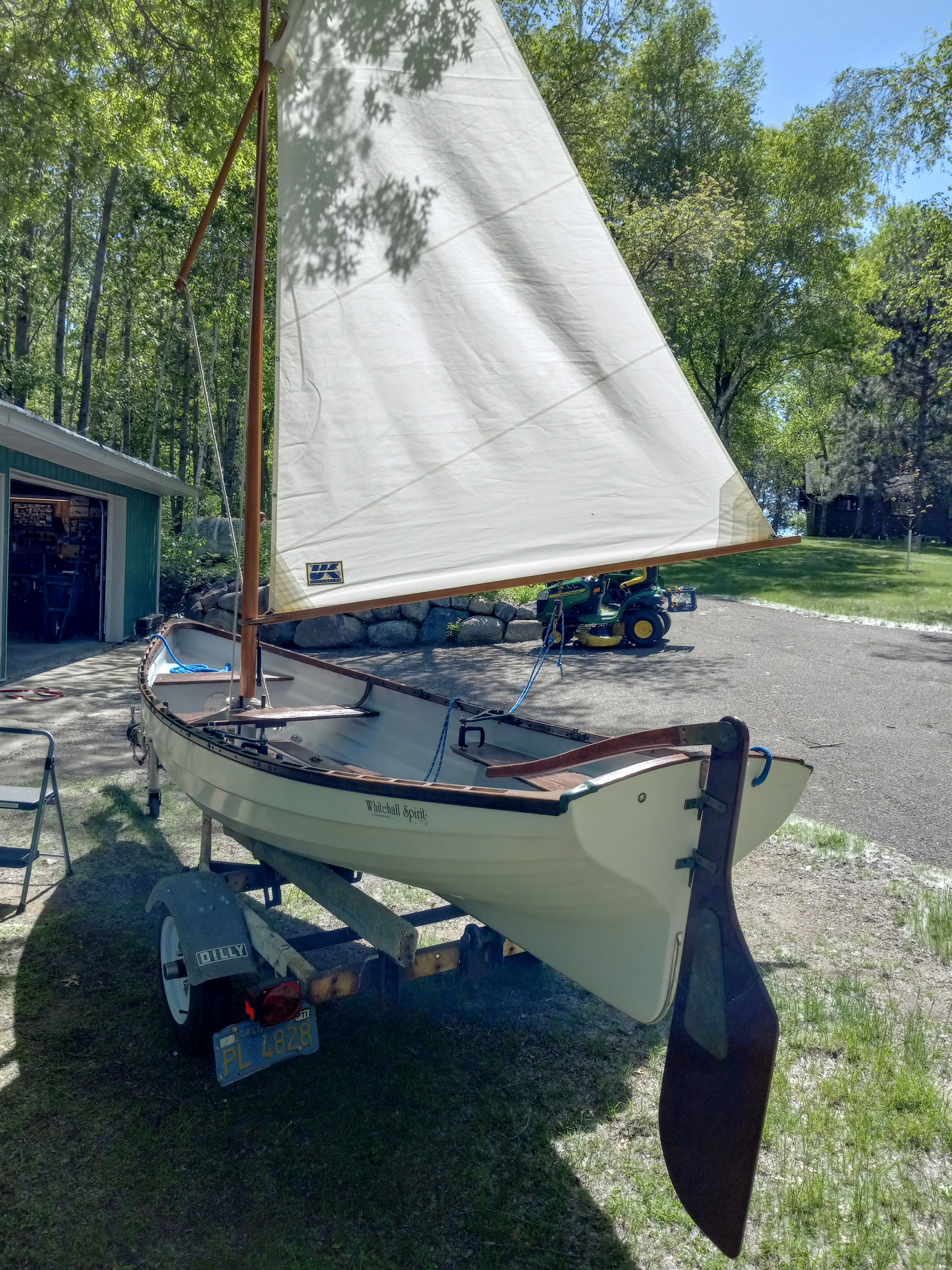 A 2005 Whitehall Spirit 14 sailboat on a trailer in a green garden setting.