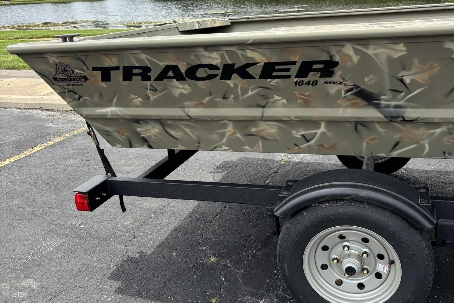 2025 Tracker Grizzly 1648 Jon boat on trailer, camouflage design, parked near water.