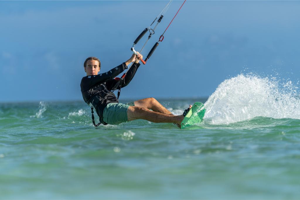 Man kiteboarding on the ocean, creating a splash in the water.
