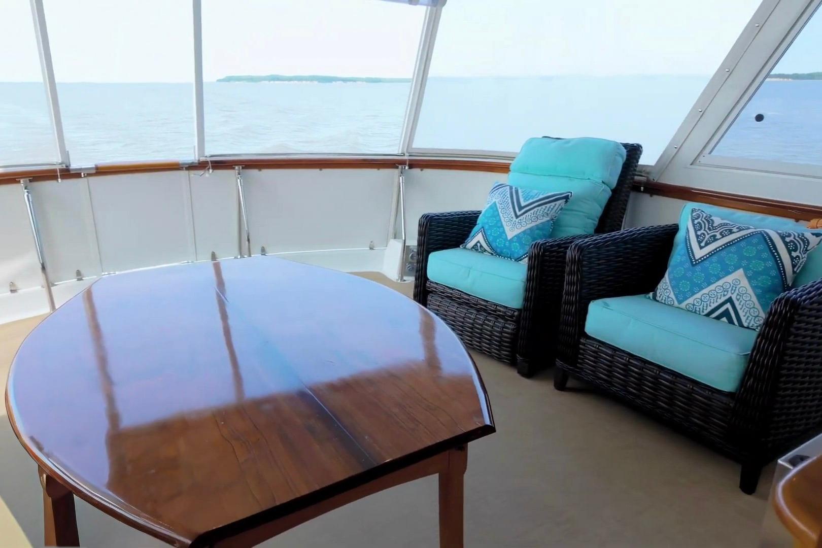 Luxurious 1980 Hatteras 70 Motor Yacht interior with ocean view, wicker chairs, and wooden table.