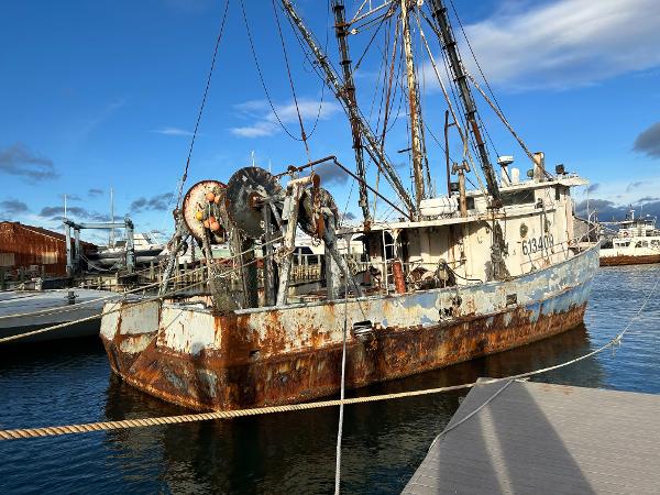 Old 1979 Custom Steel Trawler Dragger with rust, docked in a marina under a blue sky.