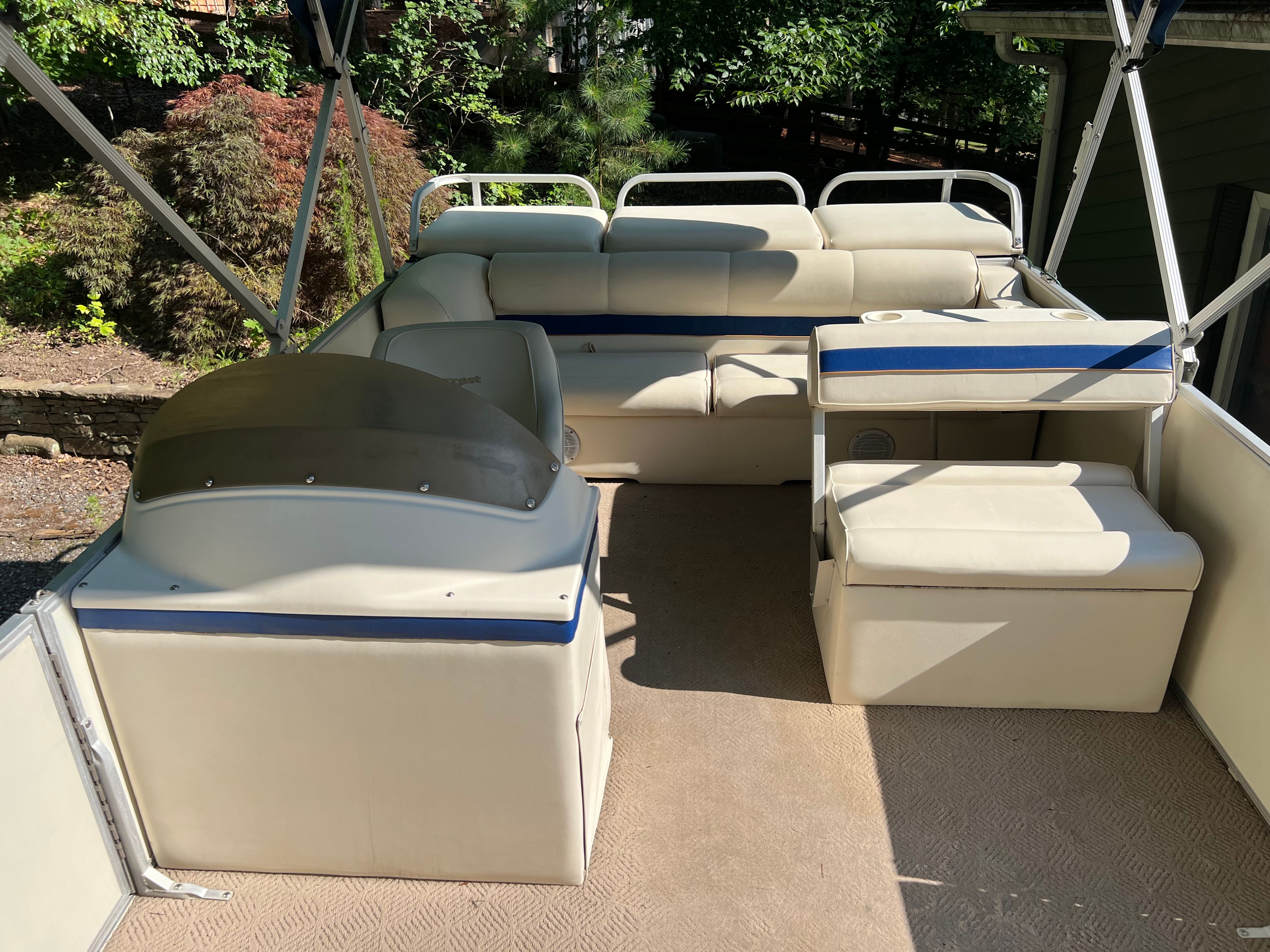 A 2003 Crest 24’ Sport pontoon boat with beige seating and blue accents, parked outdoors.