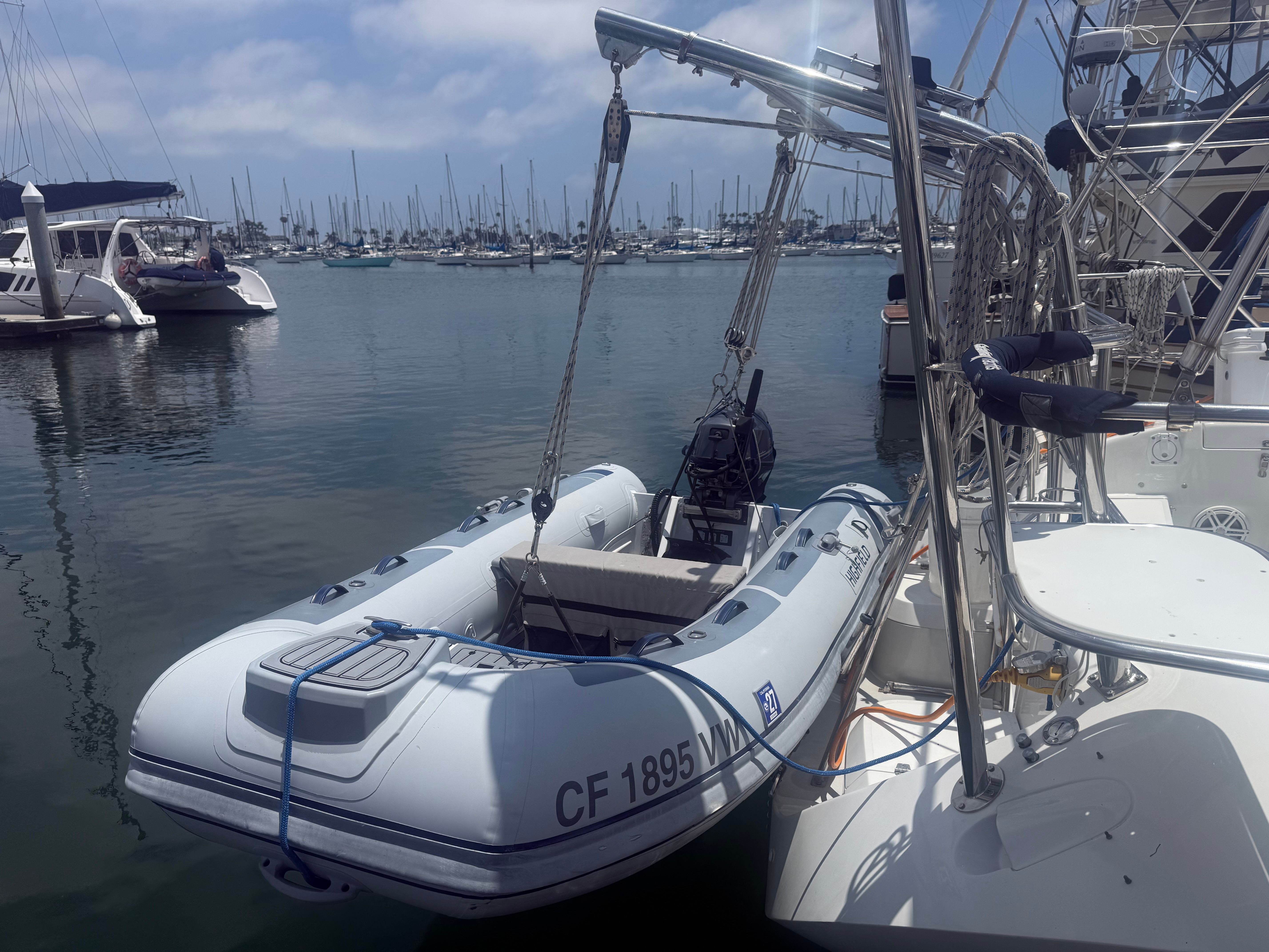 A Highfield Classic 310 inflatable boat is suspended on a davit system at the harbor.