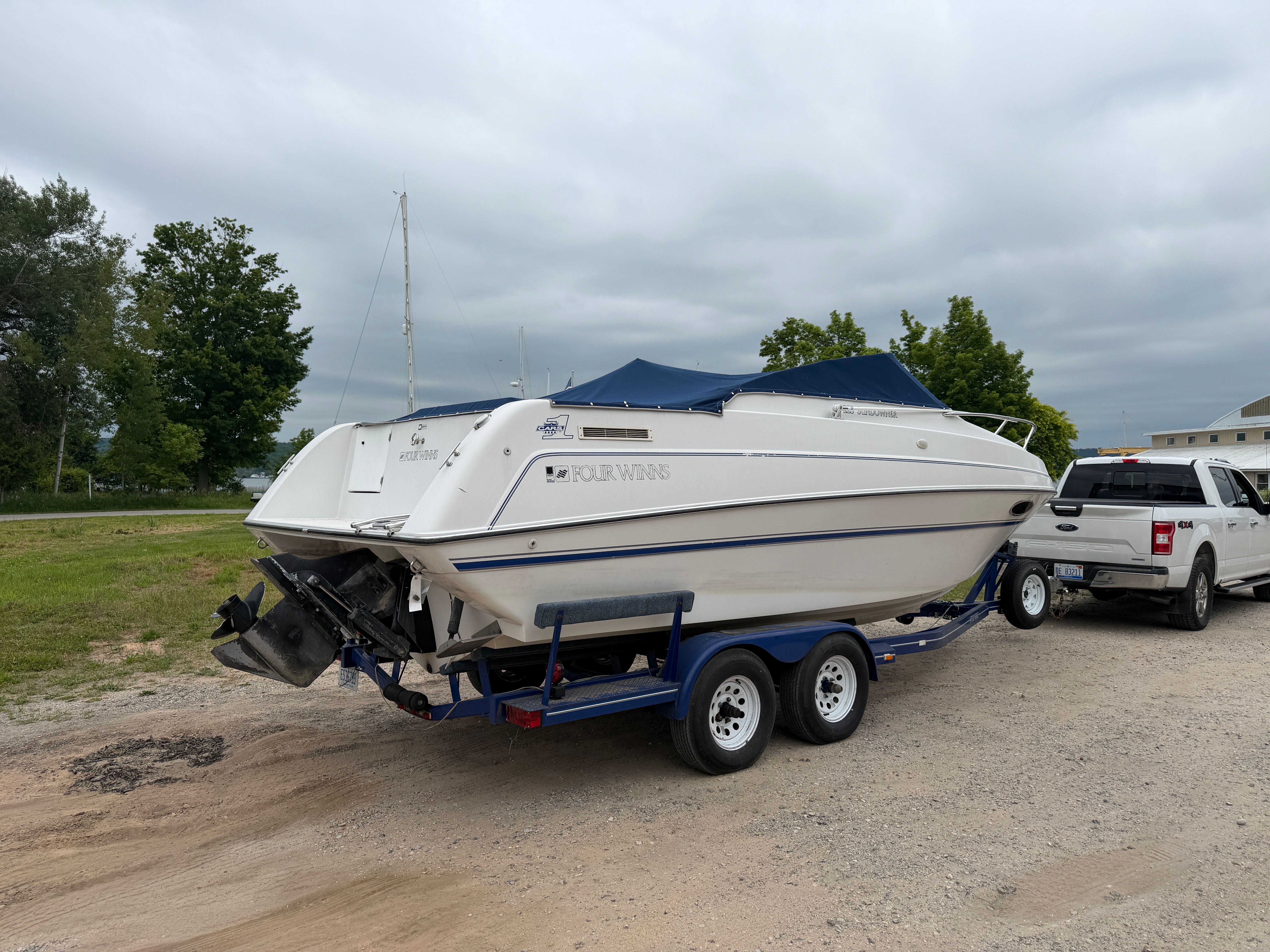 A white boat, a 1992 Four Winns 225 Sundowner, is on a trailer next to a pickup truck.