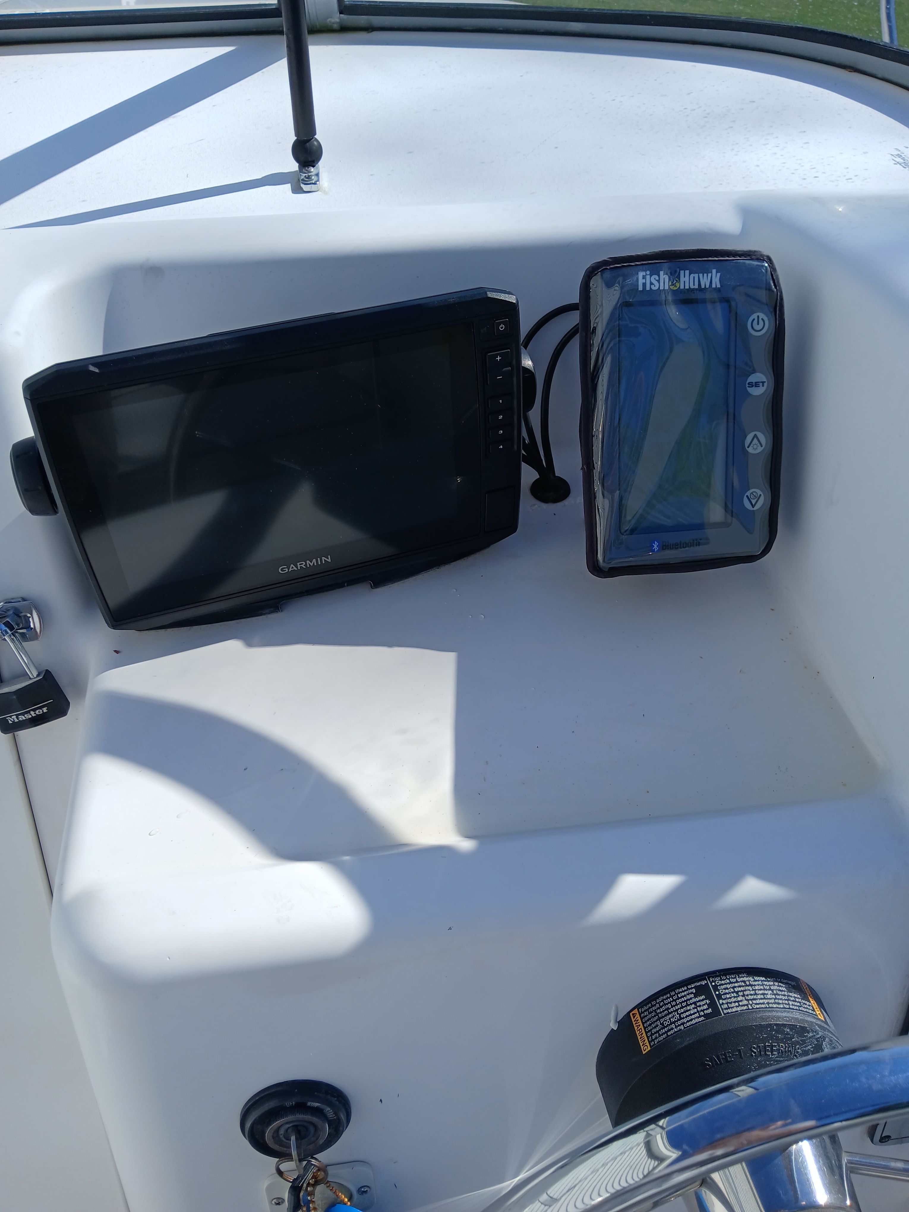 The image shows a boat's dashboard with a Garmin screen and a Fish-Hawk device.