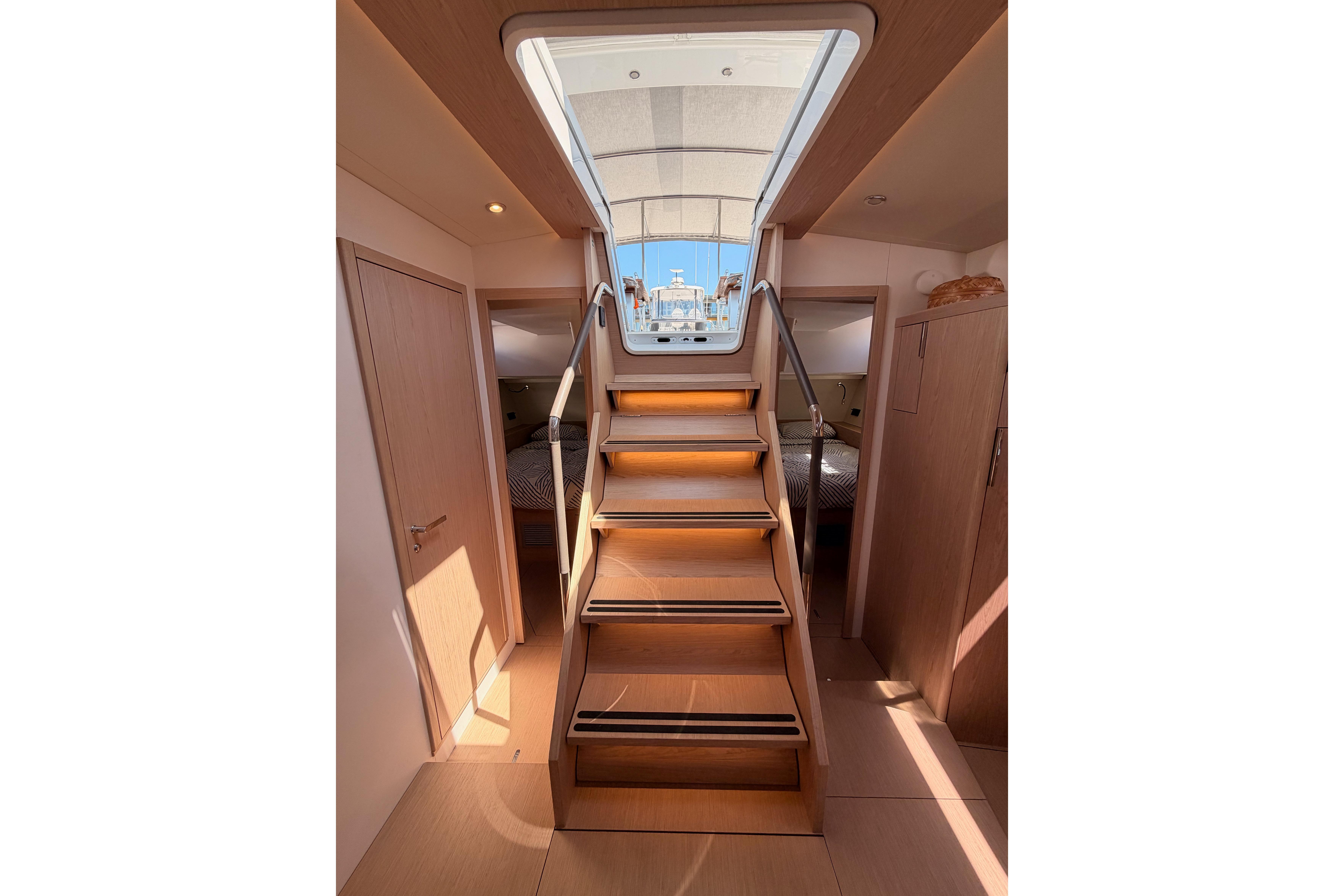 Interior view of 2022 Beneteau Oceanis Yacht 54, featuring wooden stairs and cabin access.