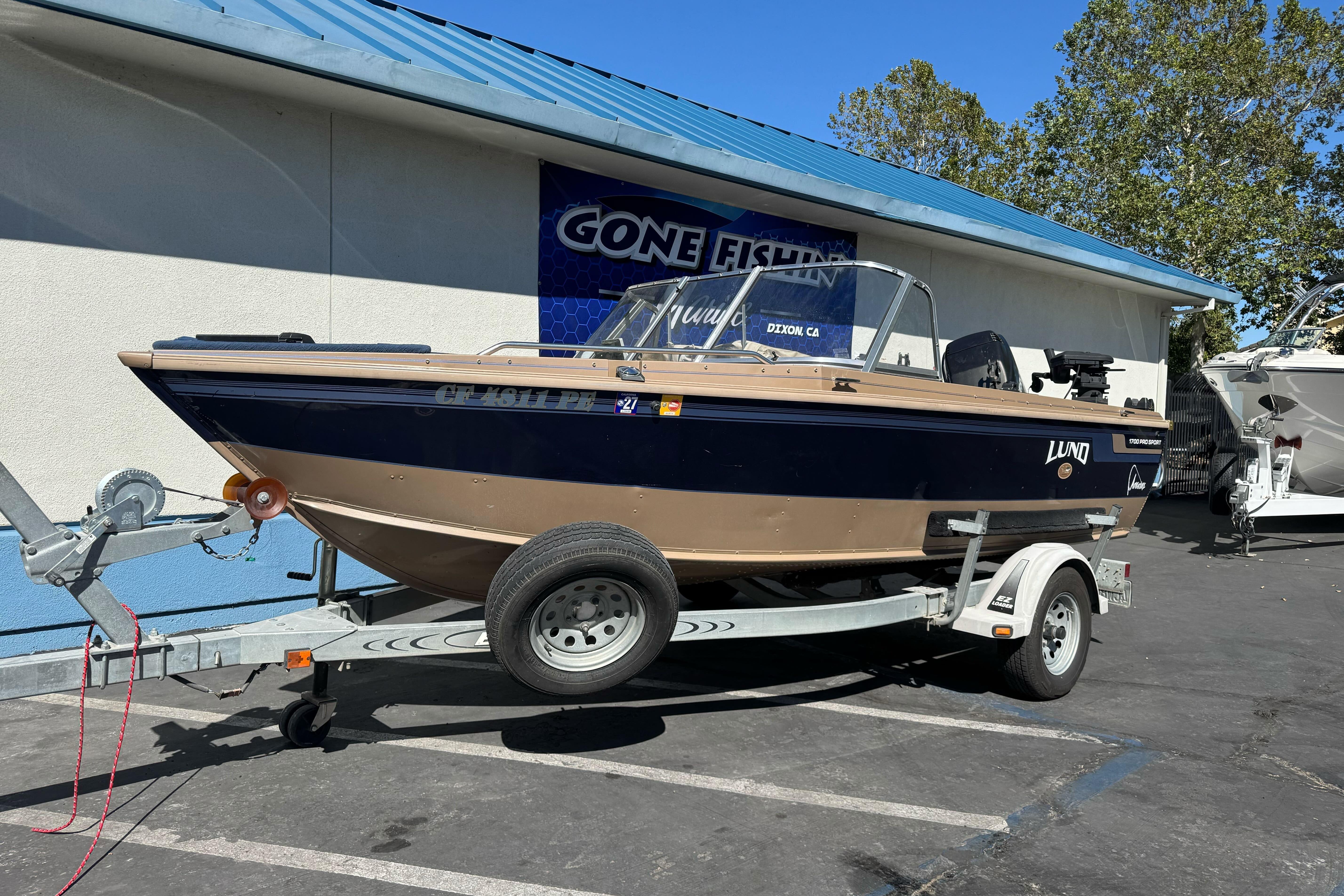 1998 Lund 1700 Pro Sport boat on trailer, parked outside a fishing store.