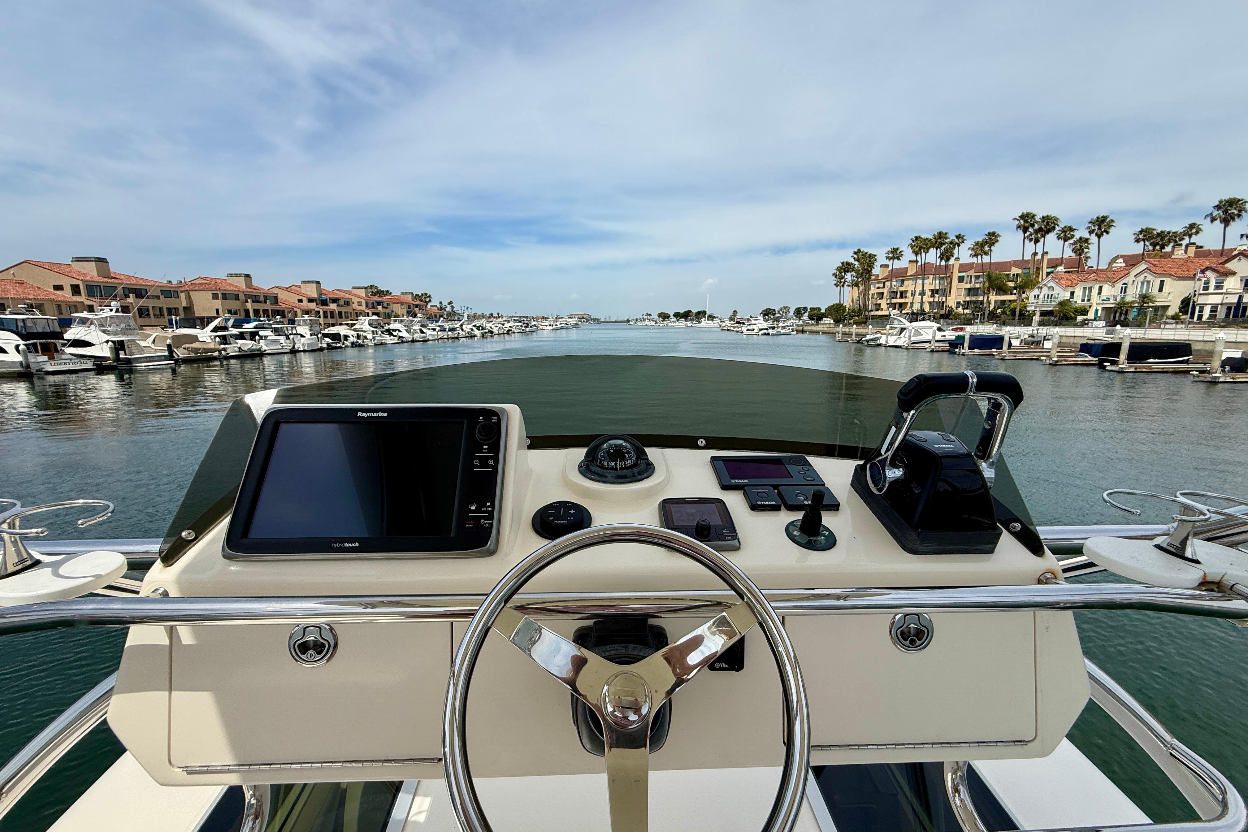 Helm view of 2012 Pursuit OS 345 Offshore boat navigating a scenic marina.
