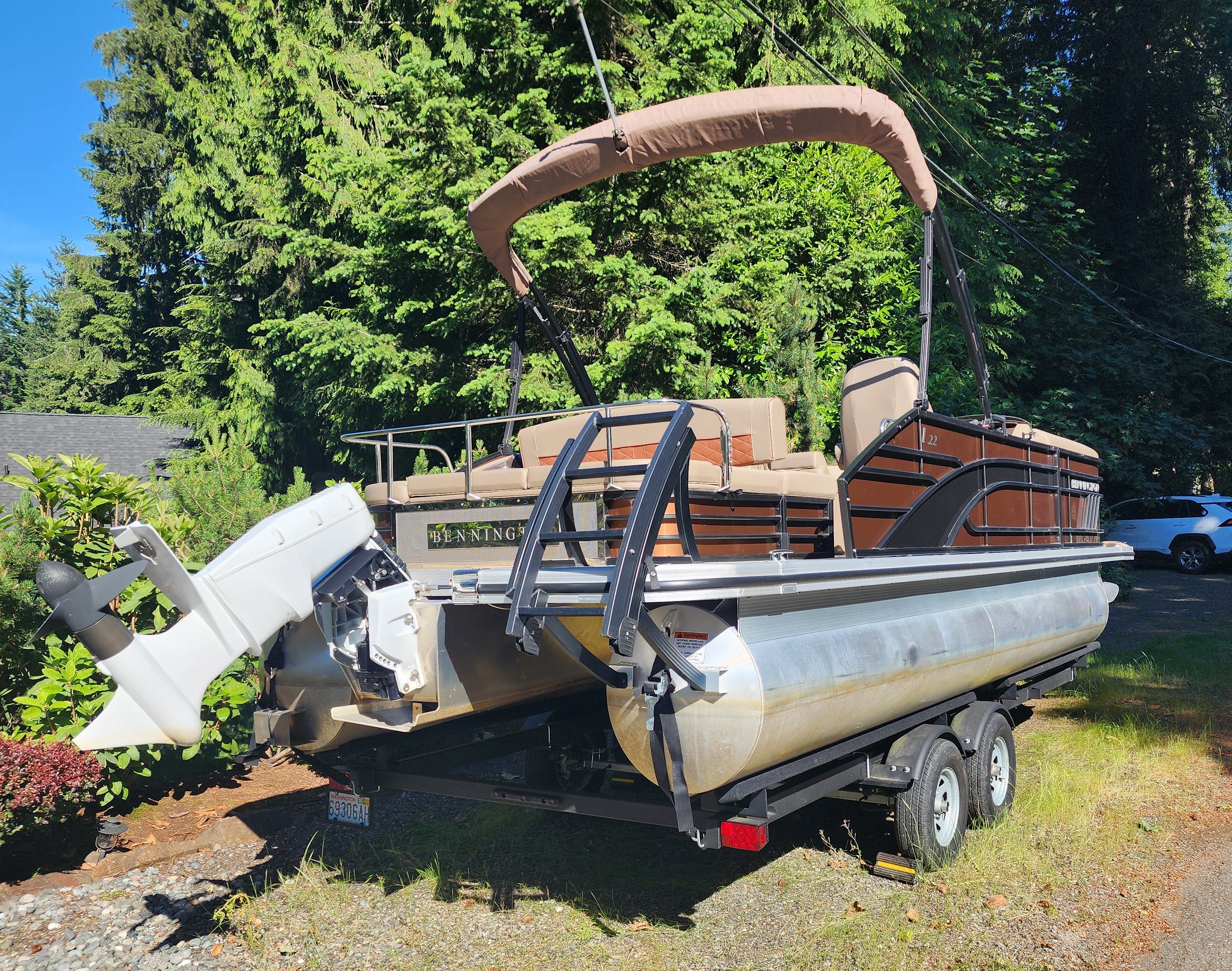A 2023 Bennington 22 LSB pontoon boat on a trailer, surrounded by trees.