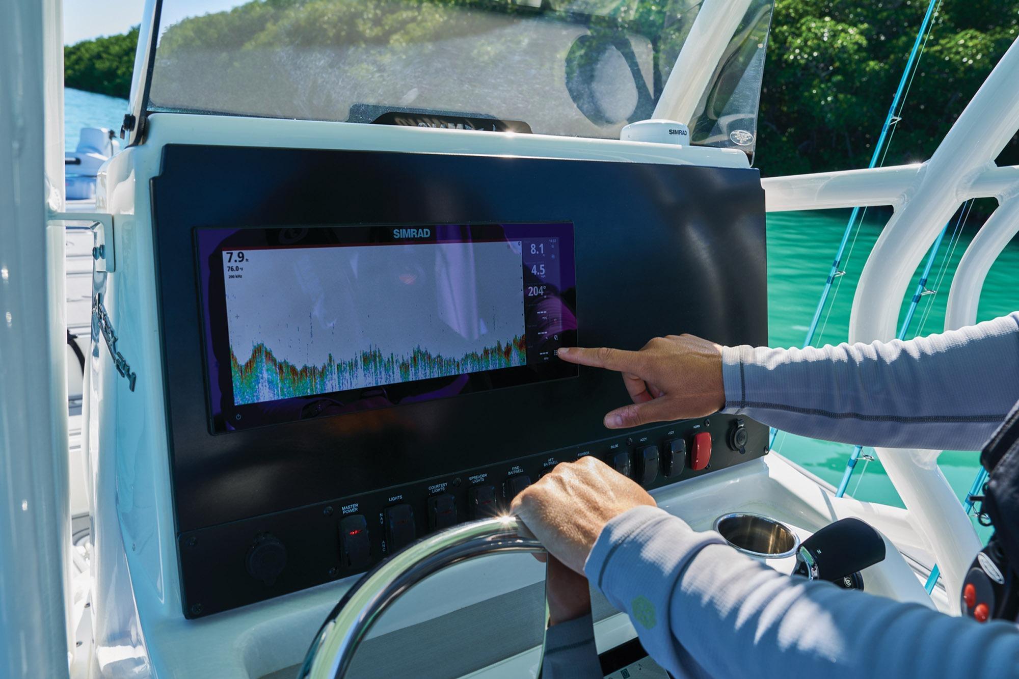 Person operating navigation system on 2026 Mako 24 APEX boat in sunny waters.