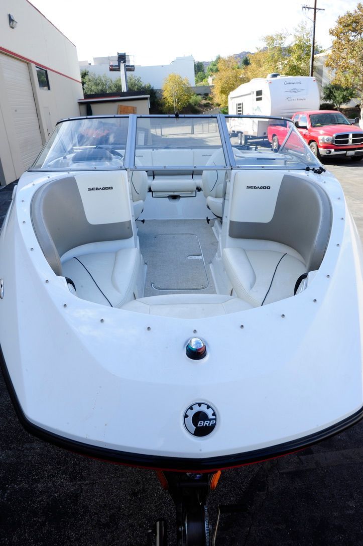 A white boat with an open cockpit is on a trailer in a parking lot.