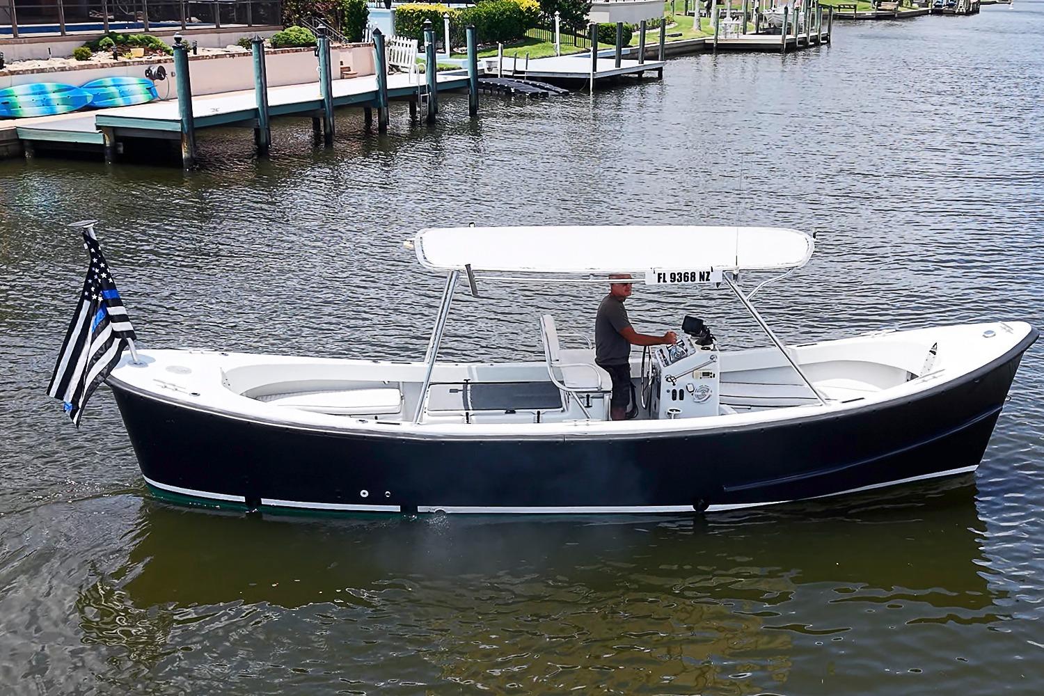 Custom 1969 boat with canopy and flag, cruising on a calm waterway.