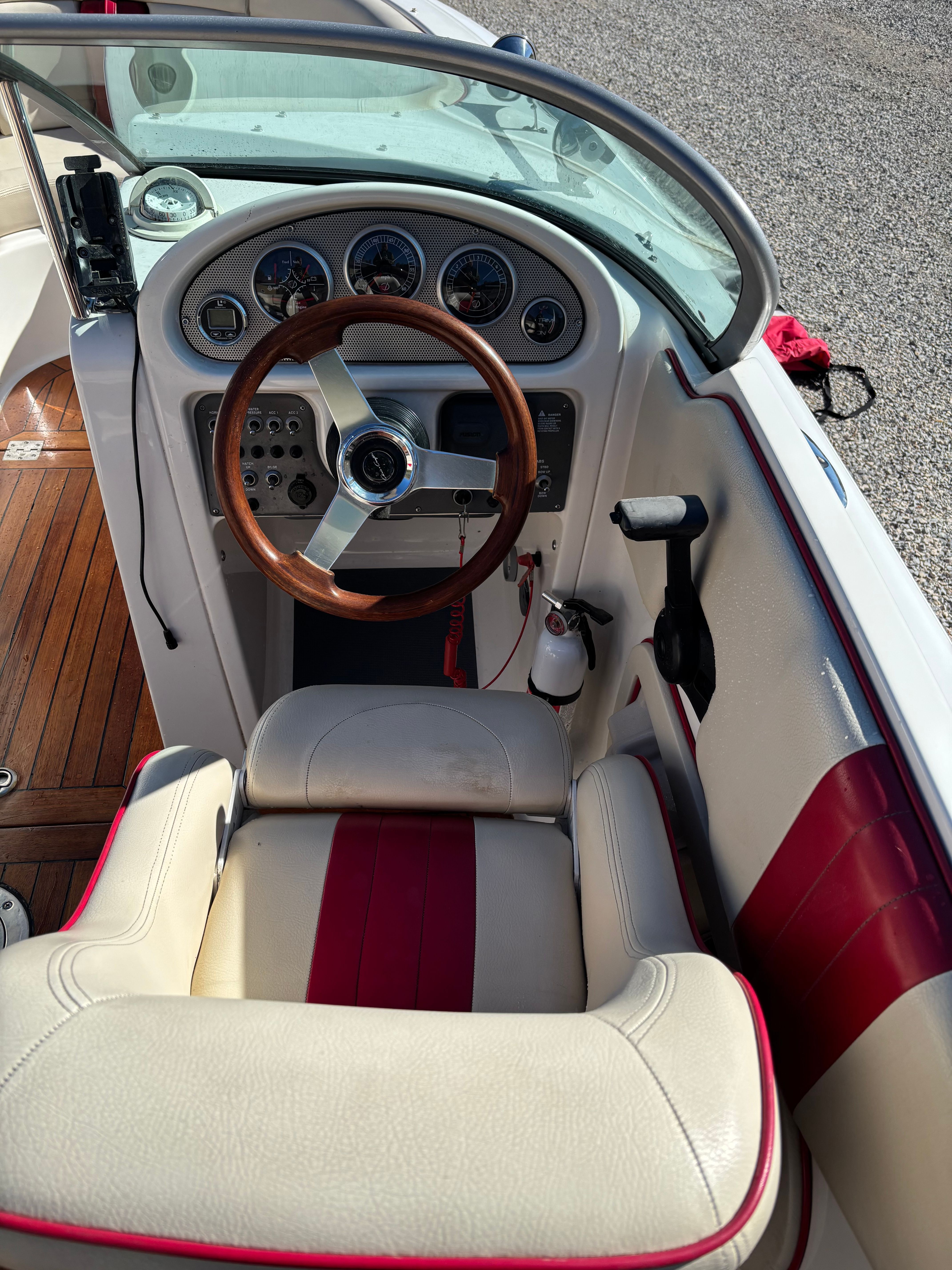 The cockpit of a 2003 Chris-Craft Launch 22 with a wooden steering wheel and red accents.