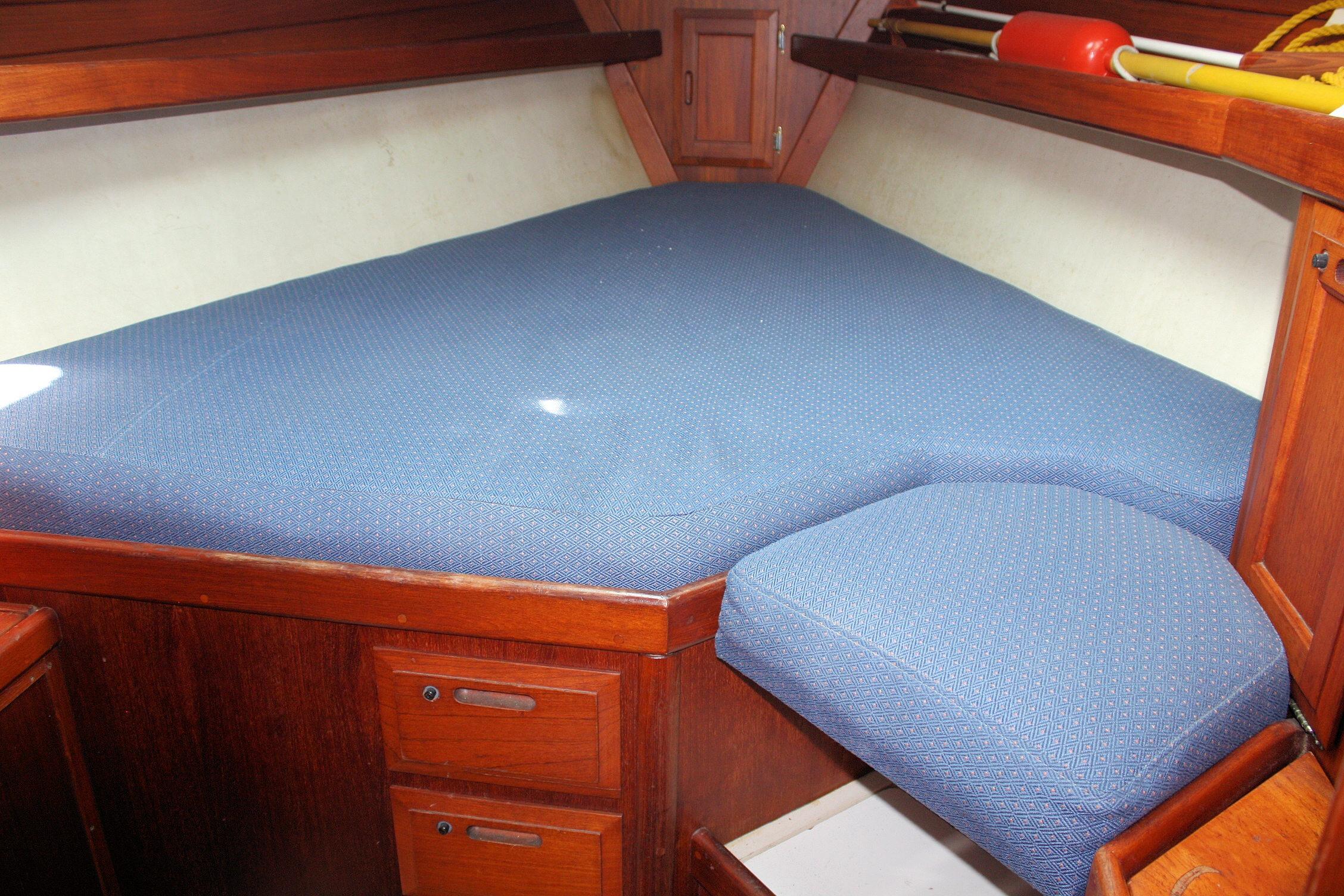 Cozy cabin interior of 1987 Ericson 38-200 sailboat with blue cushioned berth.