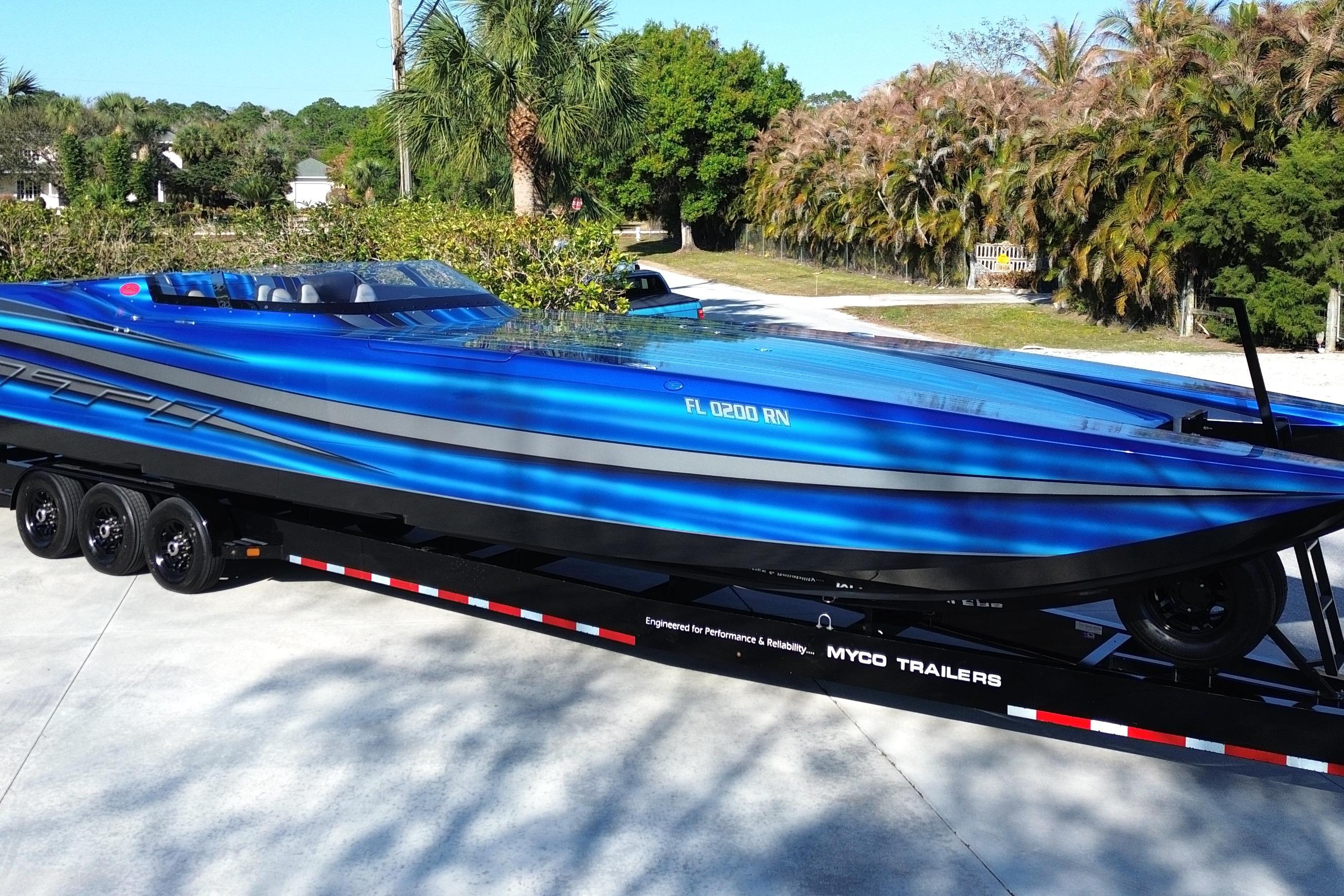 2016 MTI 44 RP speedboat in vibrant blue on a trailer, surrounded by lush greenery.