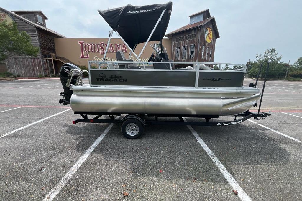2026 Sun Tracker Bass Buggy 16 XL Select pontoon boat on trailer in parking lot.