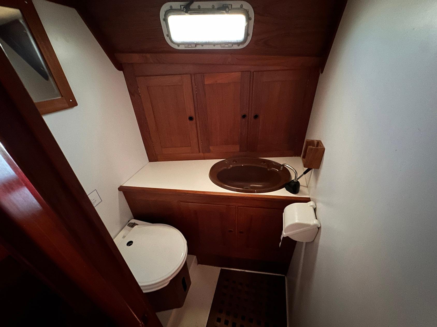 Compact wooden boat bathroom with sink, toilet, and storage cabinets, Whiting 40, 1985 model.