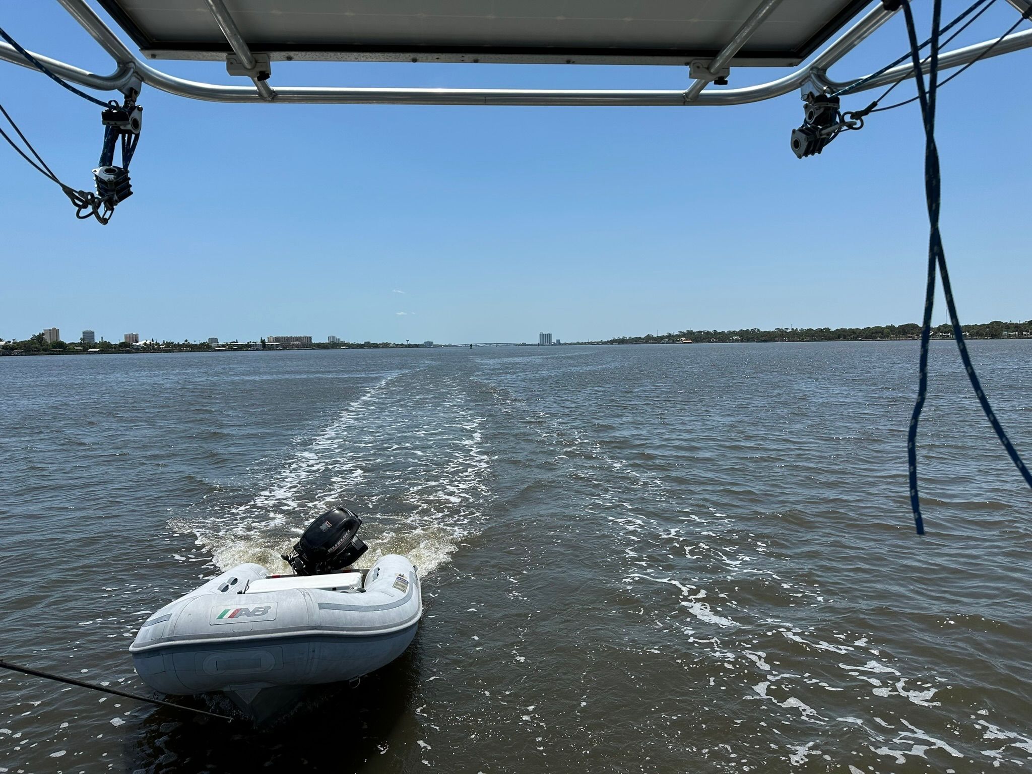 A small dinghy is being towed behind a larger boat on calm waters.