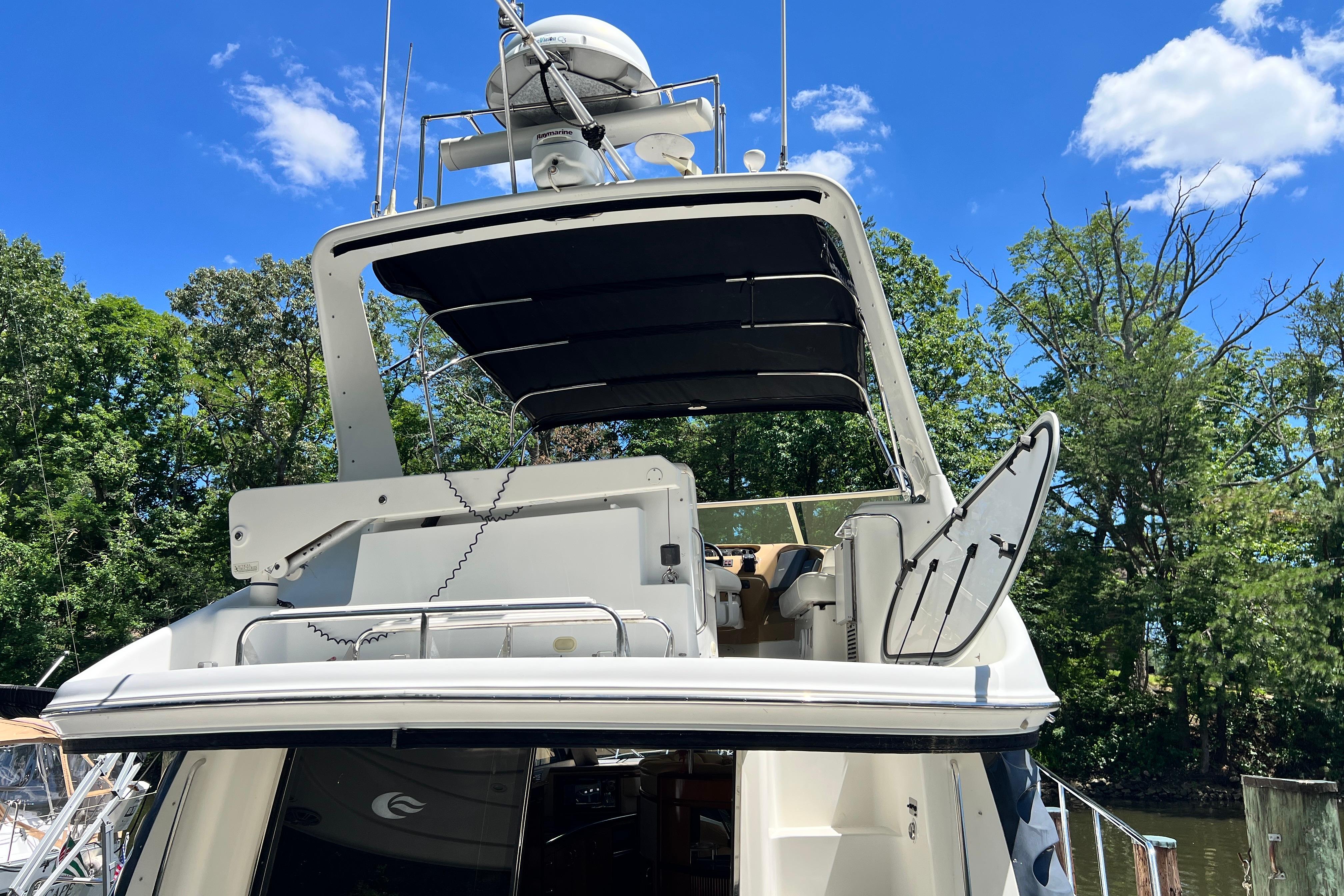 2003 Carver 450 Voyager Pilothouse yacht with open deck, surrounded by trees and blue sky.