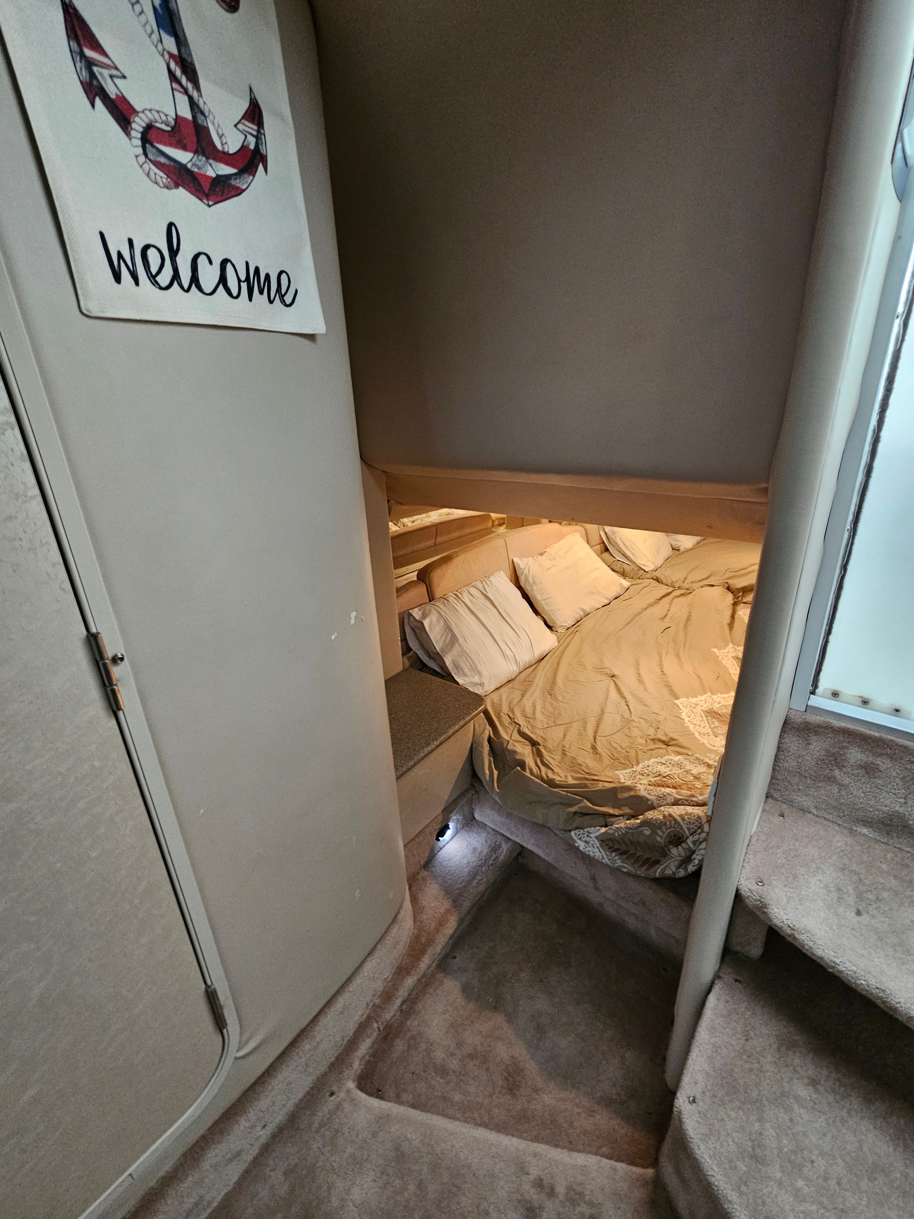 Interior of a boat cabin with a cozy bed and a "Welcome" sign.