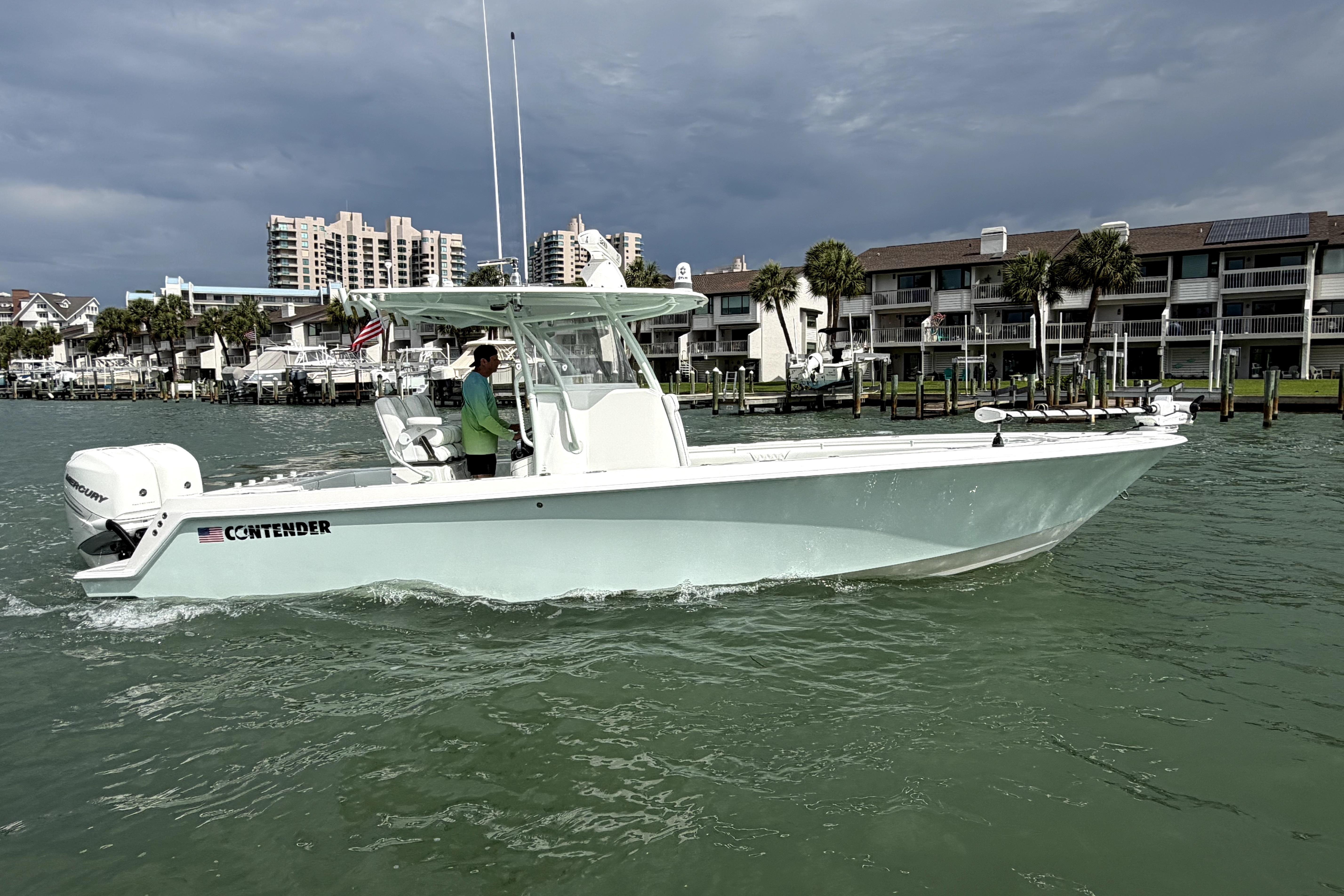 2019 Contender 30 ST boat cruising near waterfront buildings under cloudy skies.