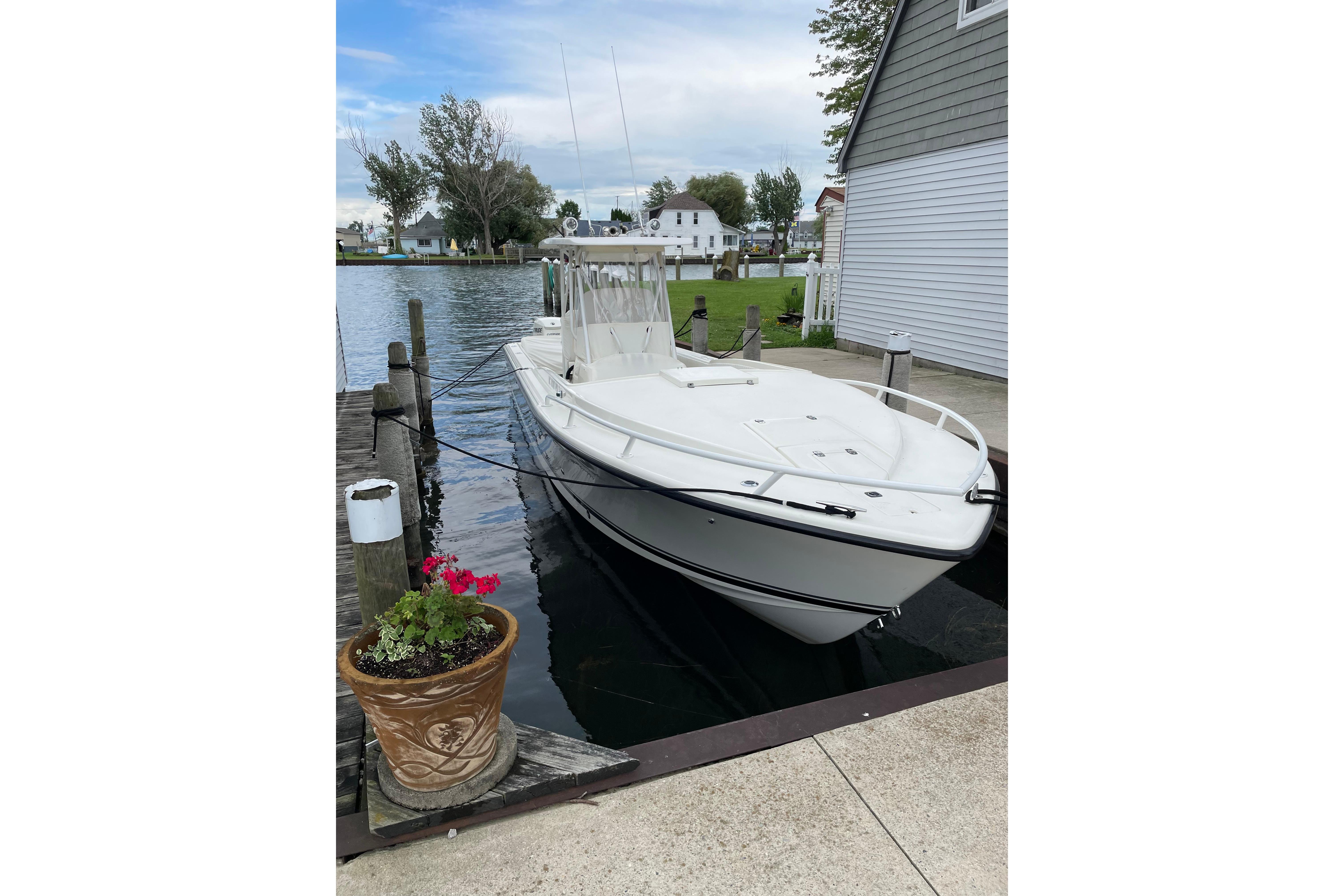 1994 Intrepid 30 Open Cuddy boat docked by a lakeside house, with potted flowers nearby.