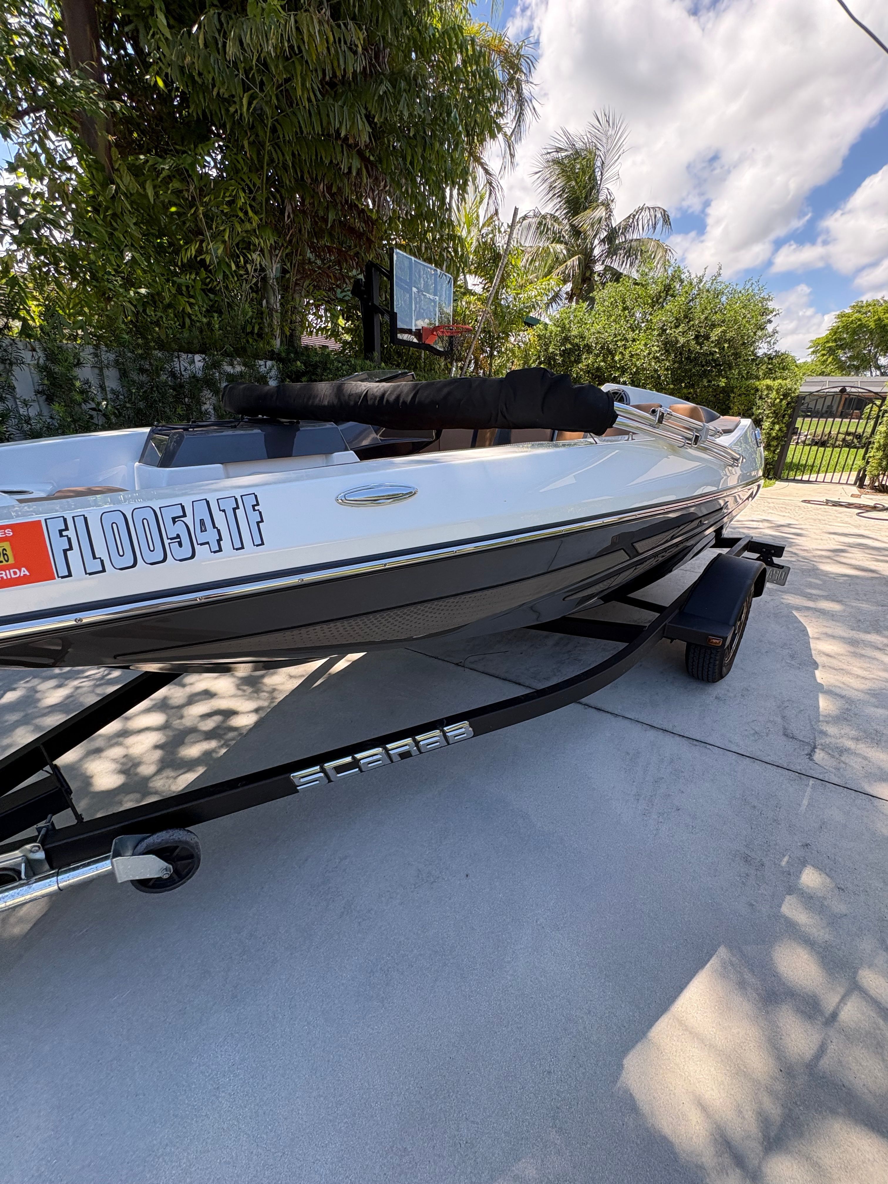 A white 2022 Scarab 165 ID boat on a trailer in a sunny driveway.